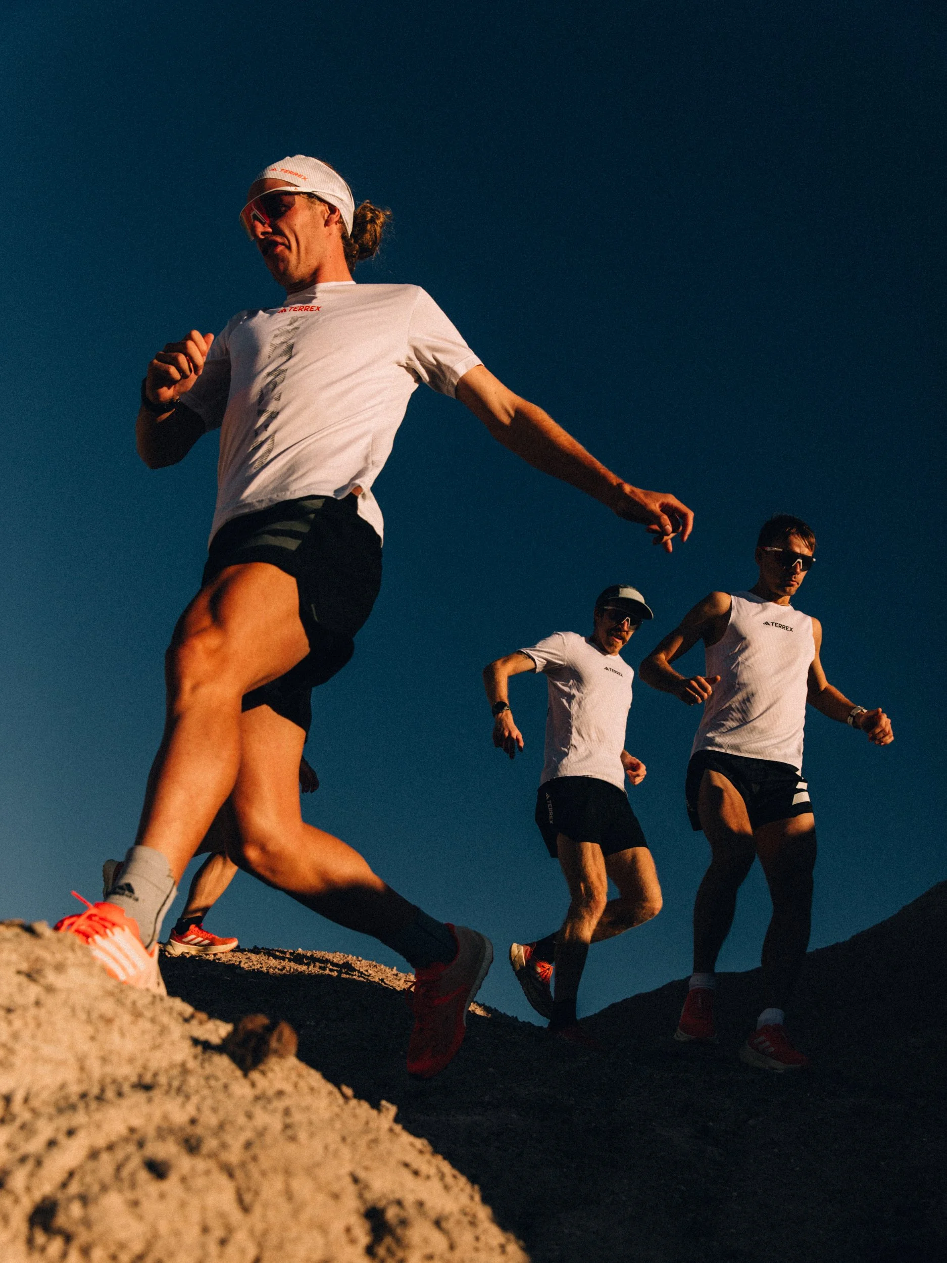 Trail runners in athletic gear running down a rocky hill under clear blue sky