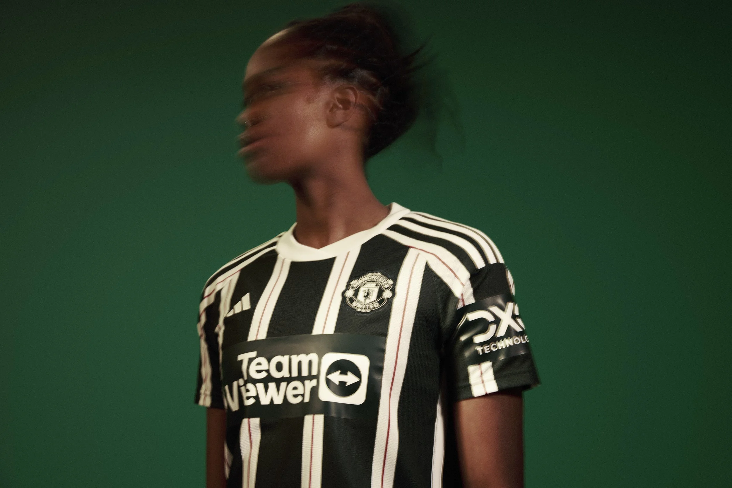 Person in black and white Manchester United jersey with blurred face on green background