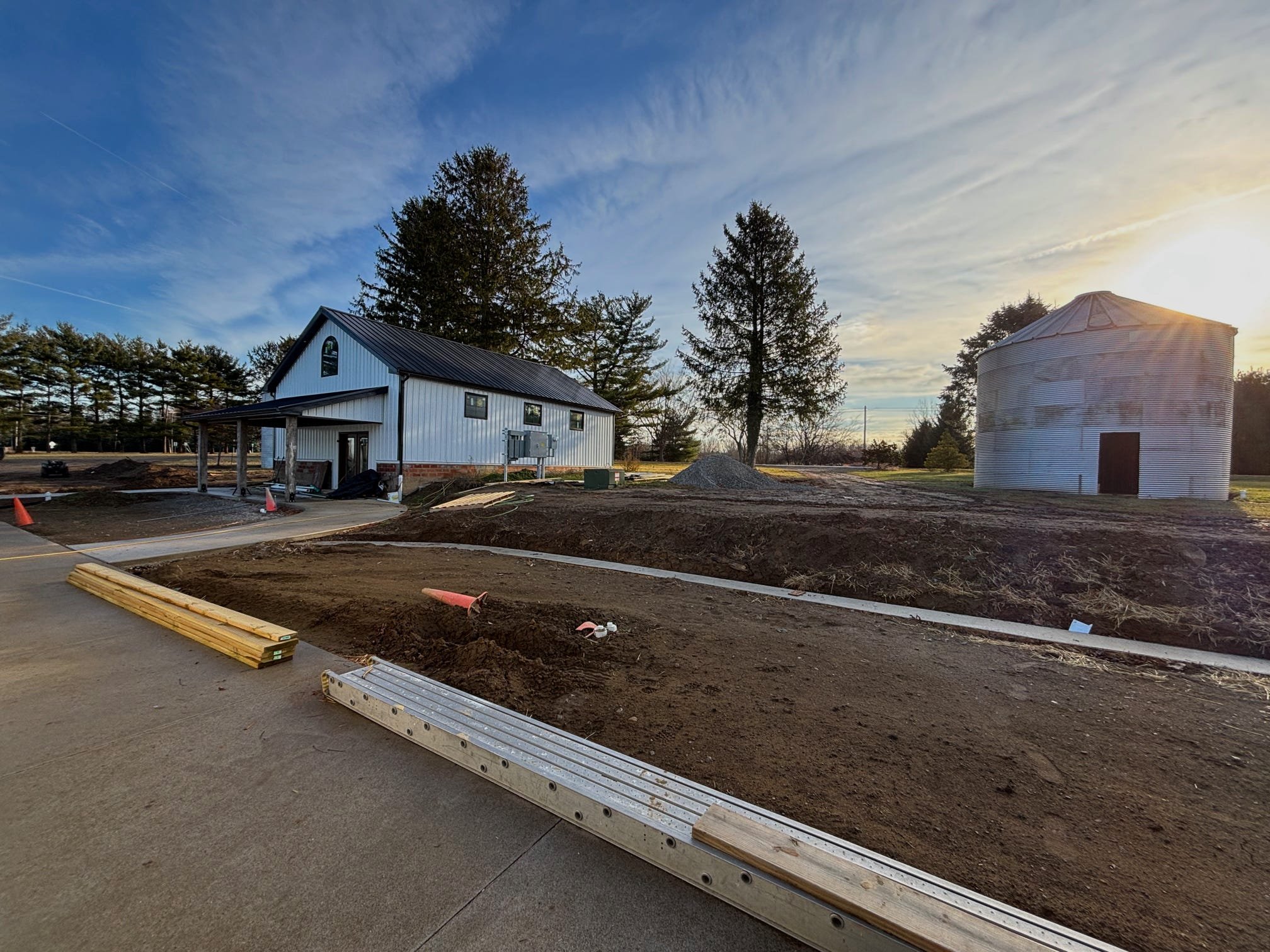 Barn and silo on farmland with construction materials in foreground and trees in background.