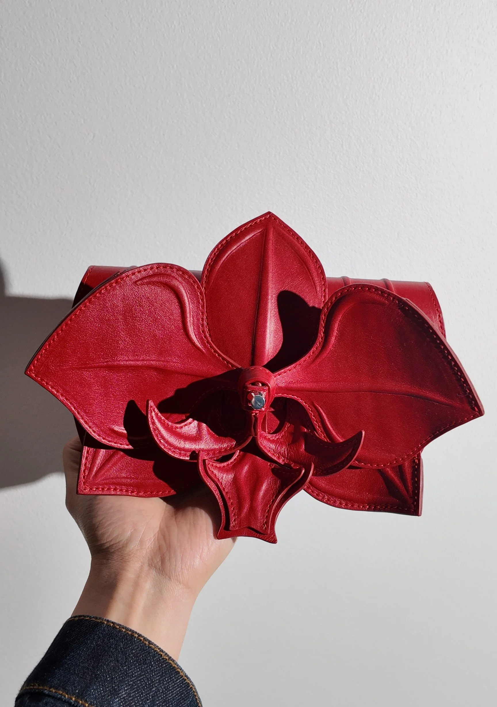 Orchid Clutch by YS Atelier held in the hand, showing its size and sculpted red petals