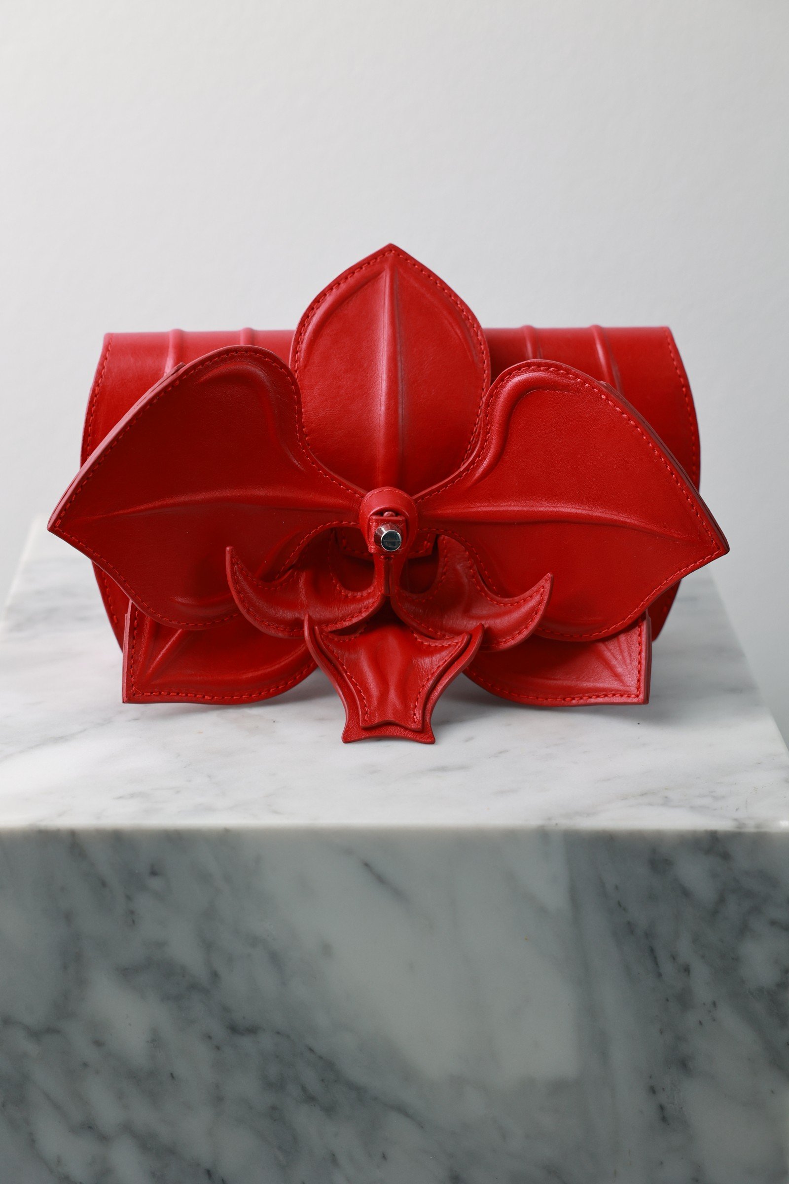 Orchid Clutch by YS Atelier: red leather clutch shaped like a moth orchid, front three-quarter view on white marble