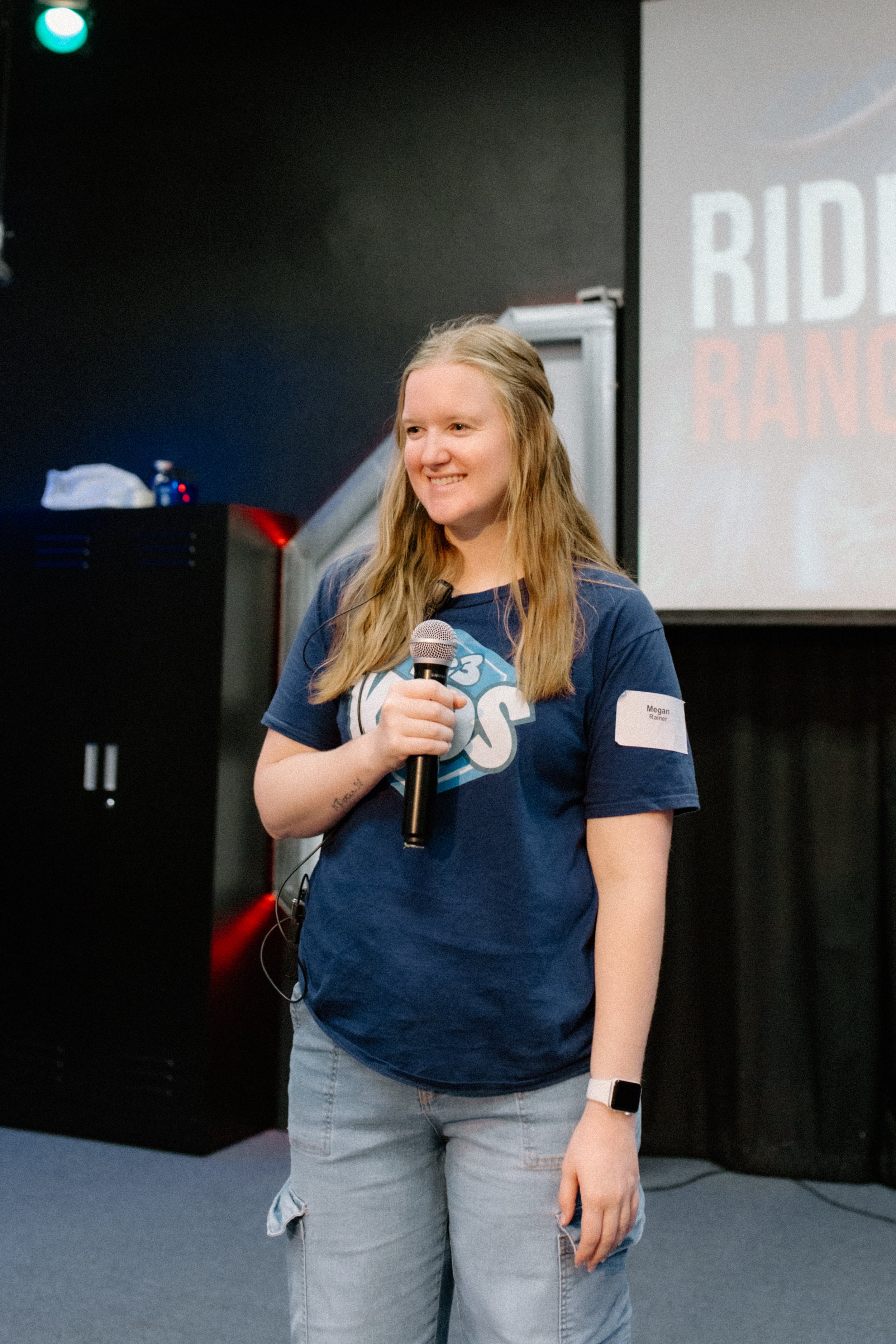 Two women smiling near a laptop at a table, with a third woman in the background at a desk.