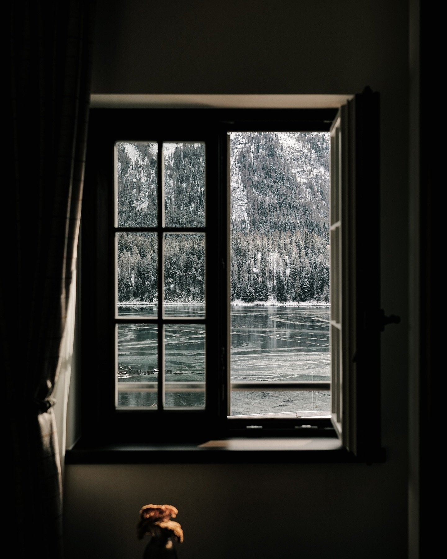 Through this window, the world unfolds in quiet contrast. Inside, warmth and stillness; outside, the frozen lake and snow-dusted peaks of St. Moritz, timeless and vast. The window becomes a threshold&mdash;a metaphor for the duality of life: comfort 