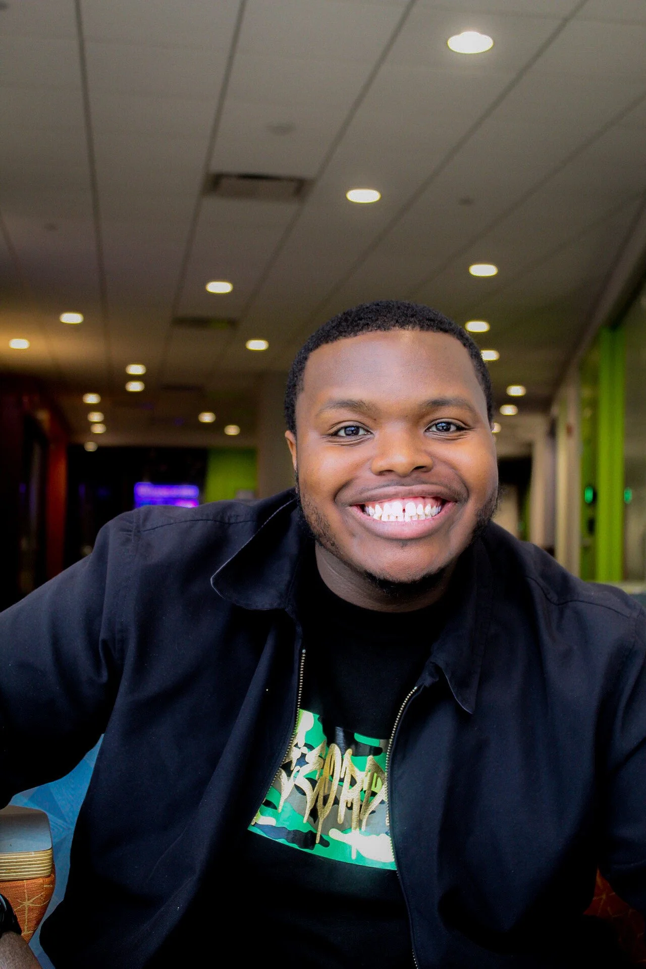 A young man smiling at the camera, wearing company shirt.