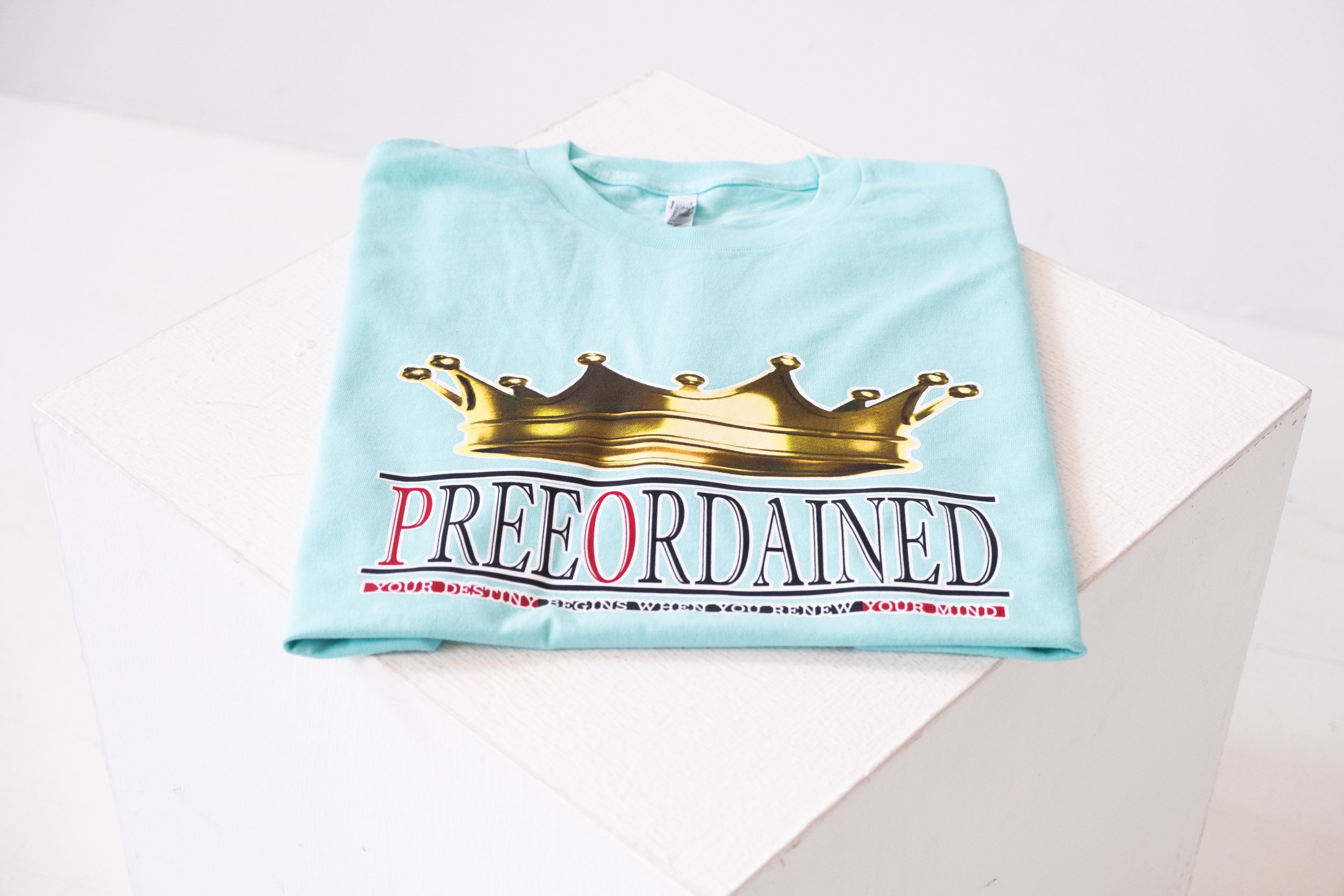 Teal colored T-shirt with a gold crown graphic and the word "PREEORDAINED" on the chest area. Underneath the logo is written "Your Destiny Begins When You Renew Your Mind".