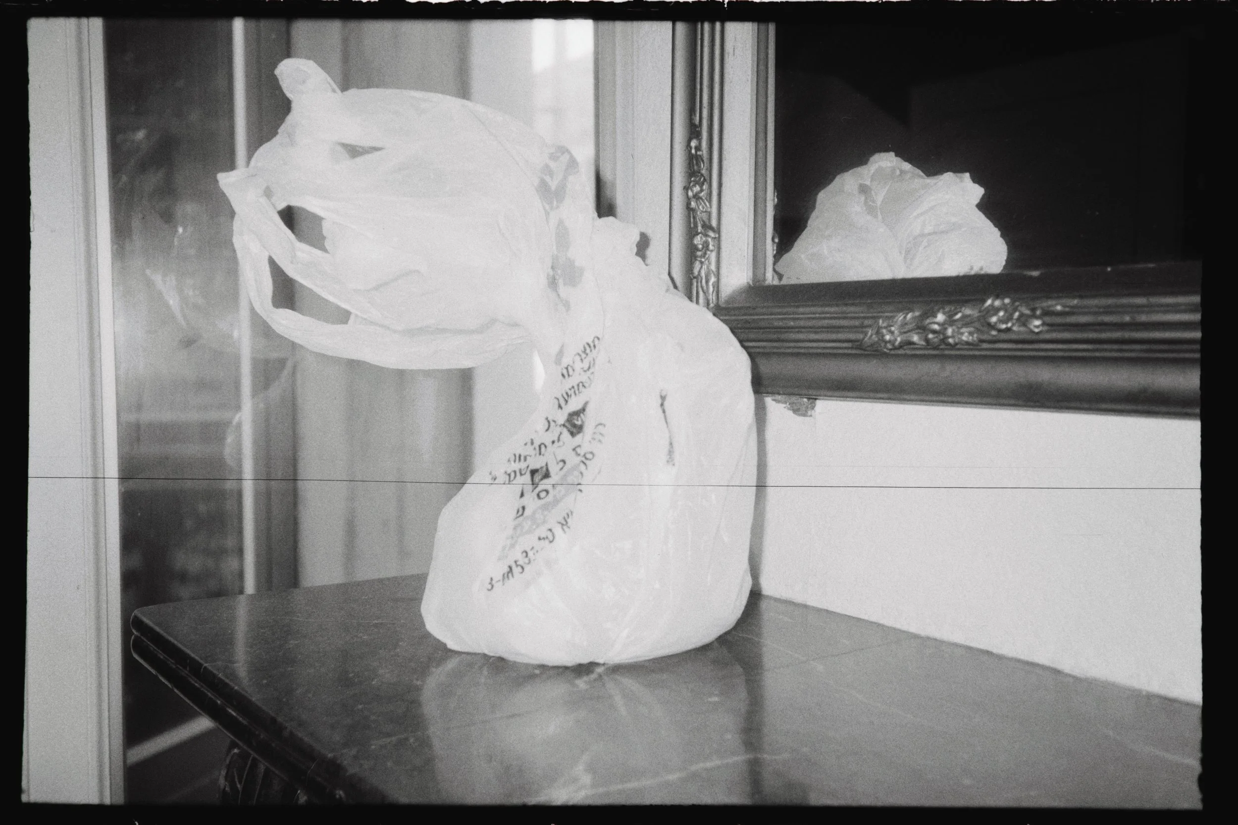 Black and white film photograph of a supermarket plastic bag containing soil, photographed in residency at Fraise, Montpellier, for the art project Common Ground (2025).