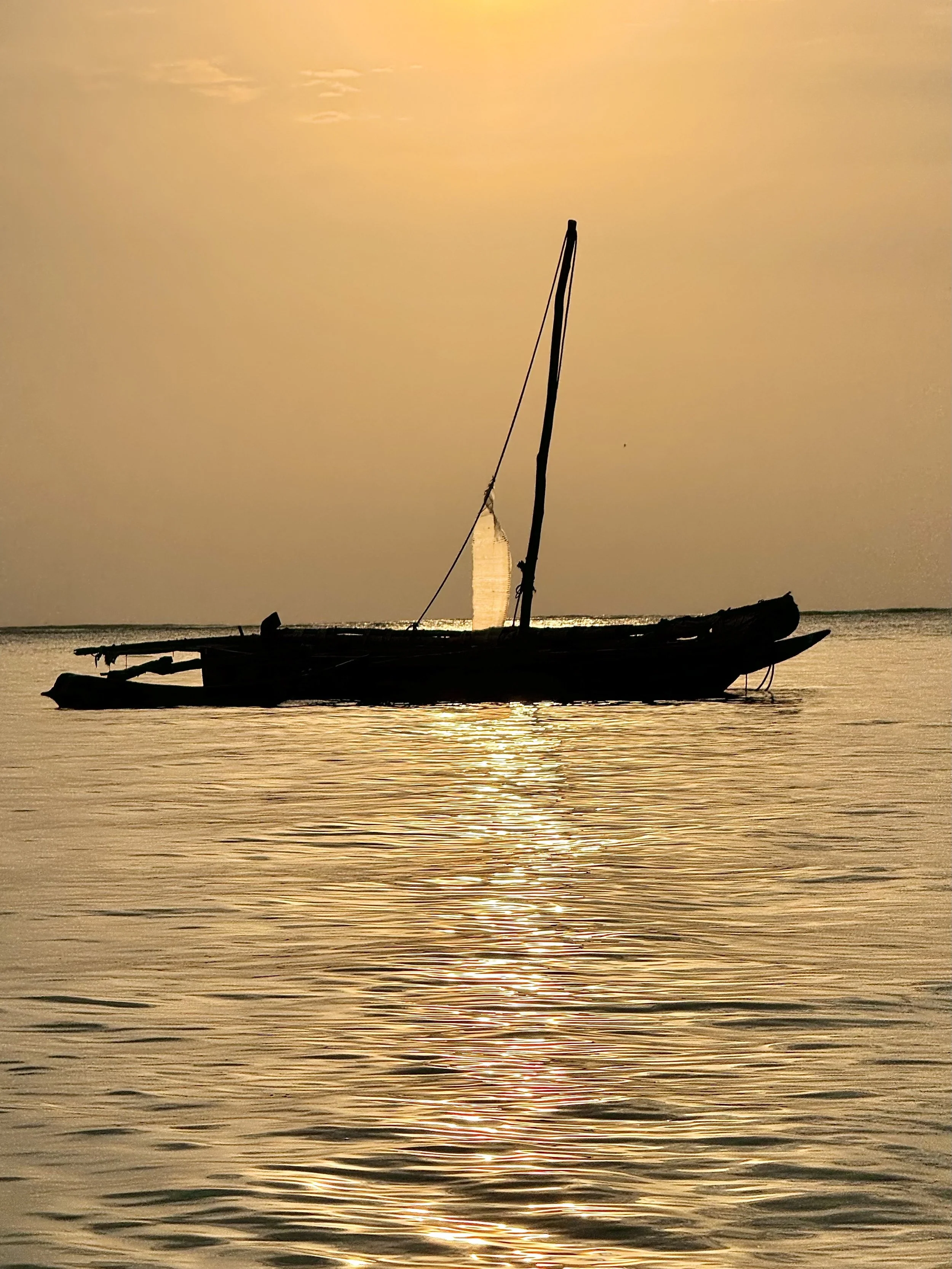 Sailboat at sunset on calm water with golden light reflecting across the ocean.