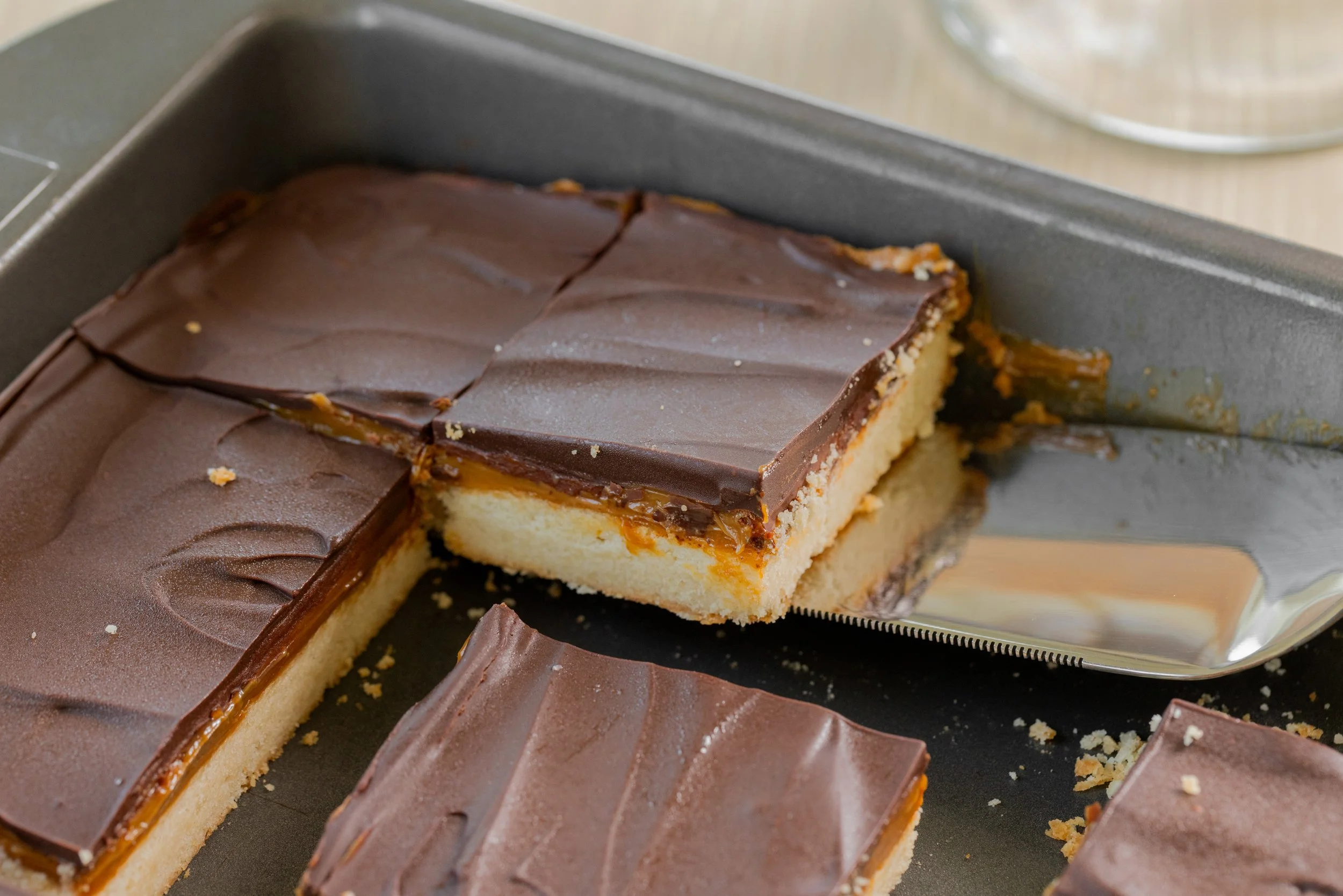 Four pieces of Millionaire's Shortbread displayed on a glass cake stand. Three delicious layers - buttery shortbread, rich creamy caramel and dark bittersweet chocolate.