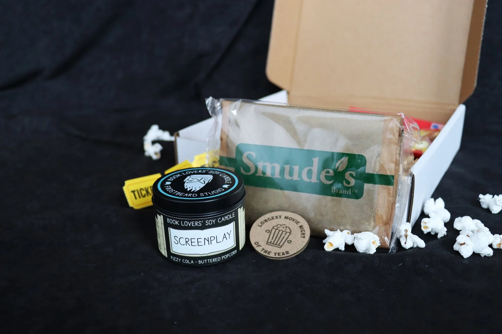 Small candle tin labeled "fizzy cola and buttered popcorn" scent. Bag of microwave popcorn labeled "Smude's Brand". Token labeled "Longest Movie Night of the Year."