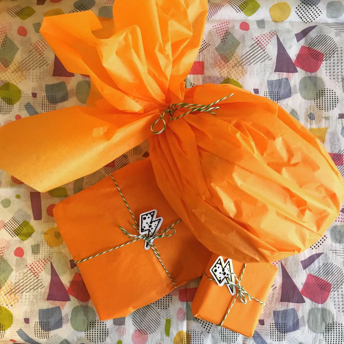 Three parcels wrapped in bright orange tissue sit on a terazzo-print tissue paper background.
