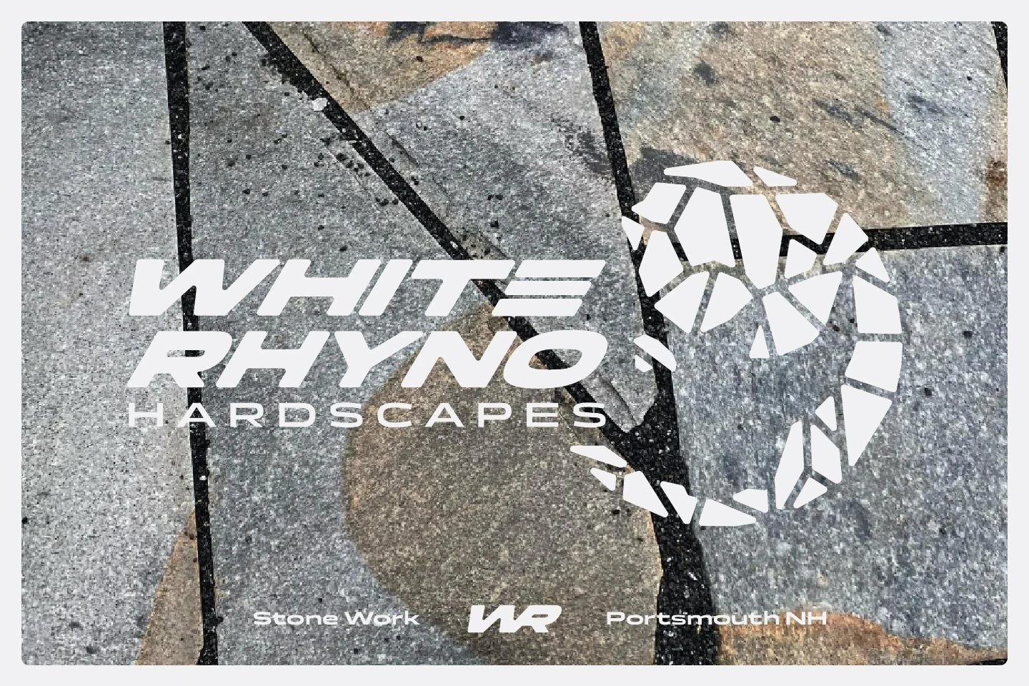 Logo for White Rhyno Hardscapes that features a custom rhino illustration balanced with a modern type lockup in light stone gray, on a photo of one of their patios featuring an irregular fieldstone patio.
