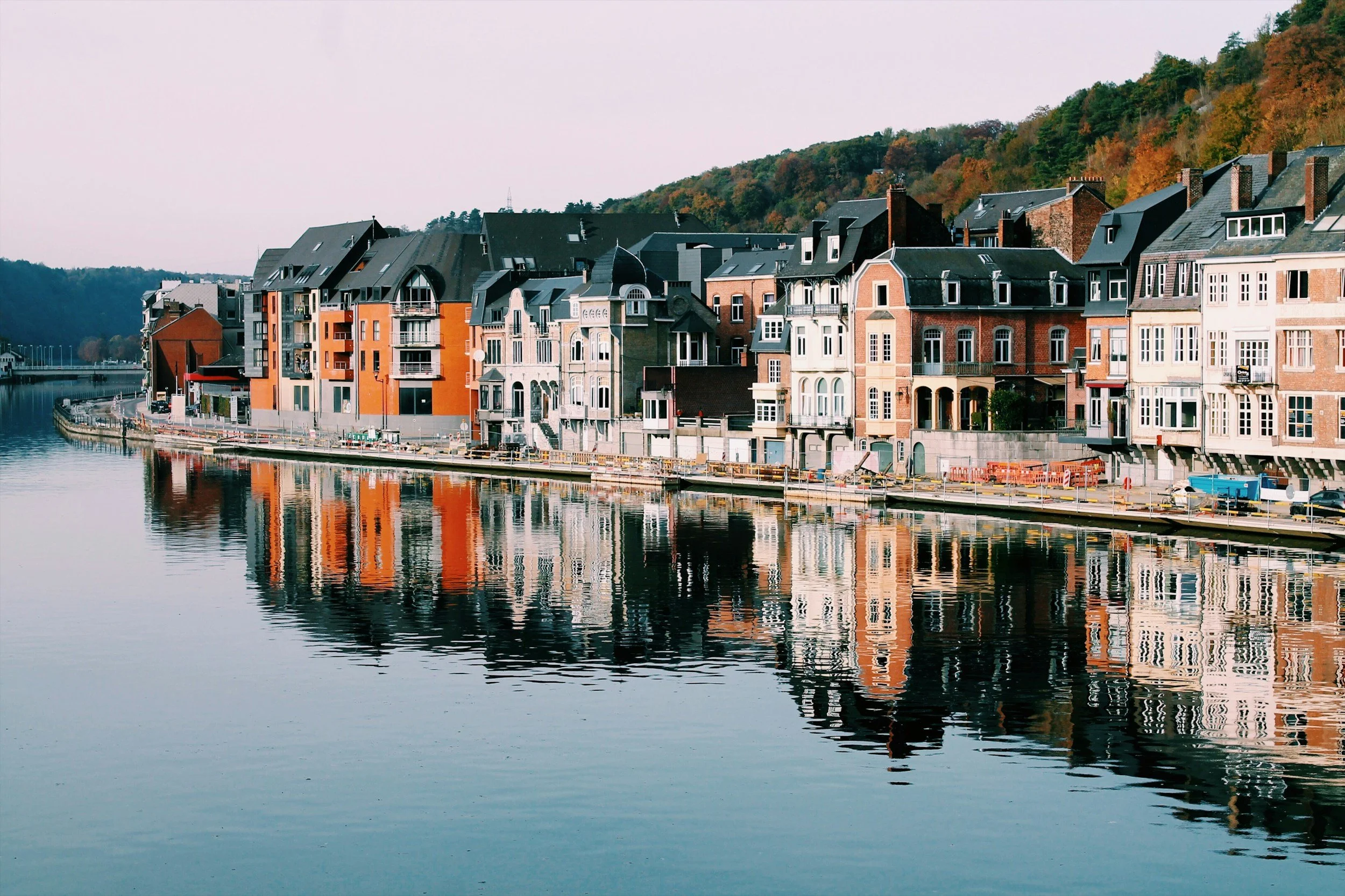 Colorful row of houses along a river with trees on a hillside in the background.