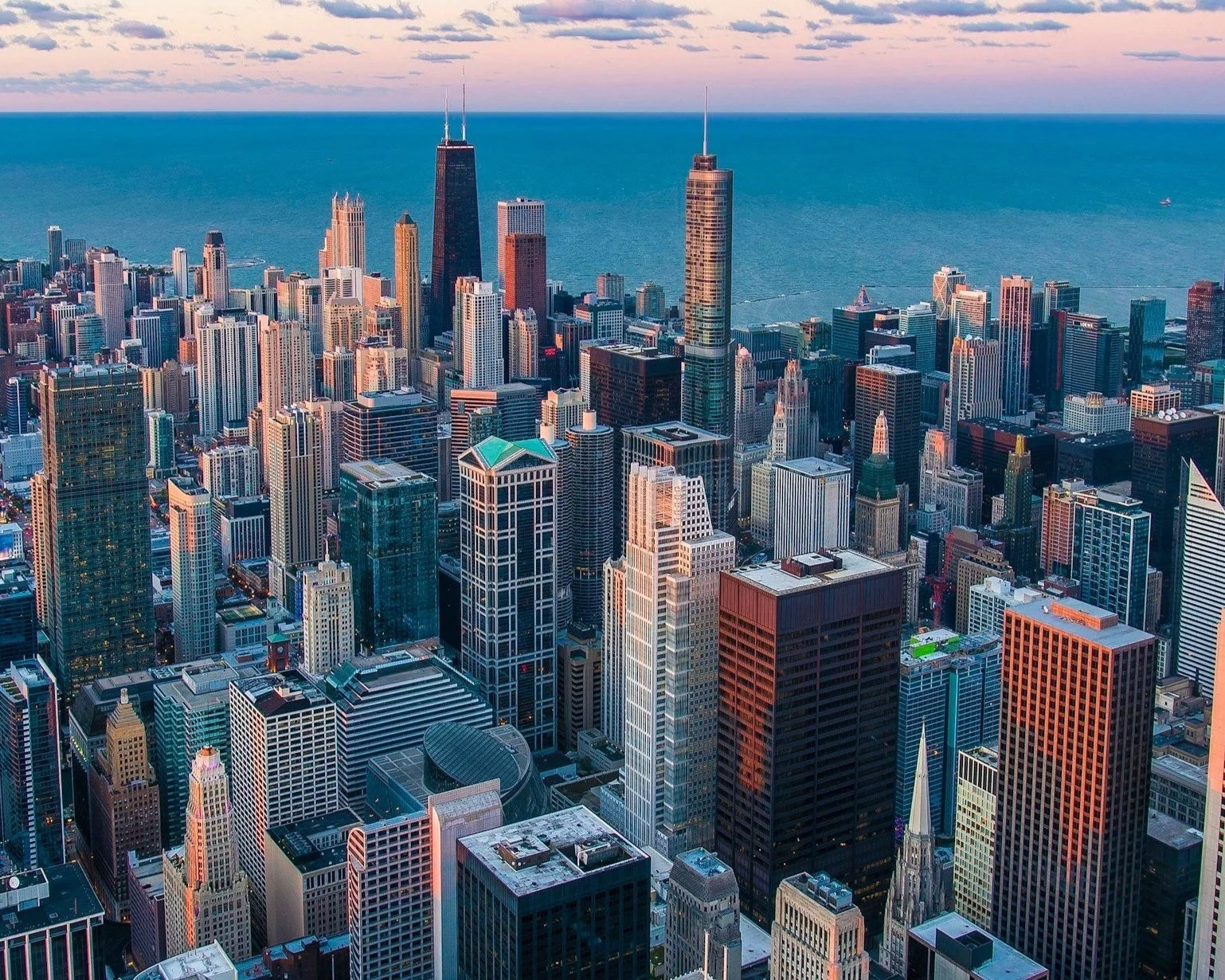 Aerial view of a city skyline with numerous tall skyscrapers overlooking a large body of water, with a partly cloudy sky.
