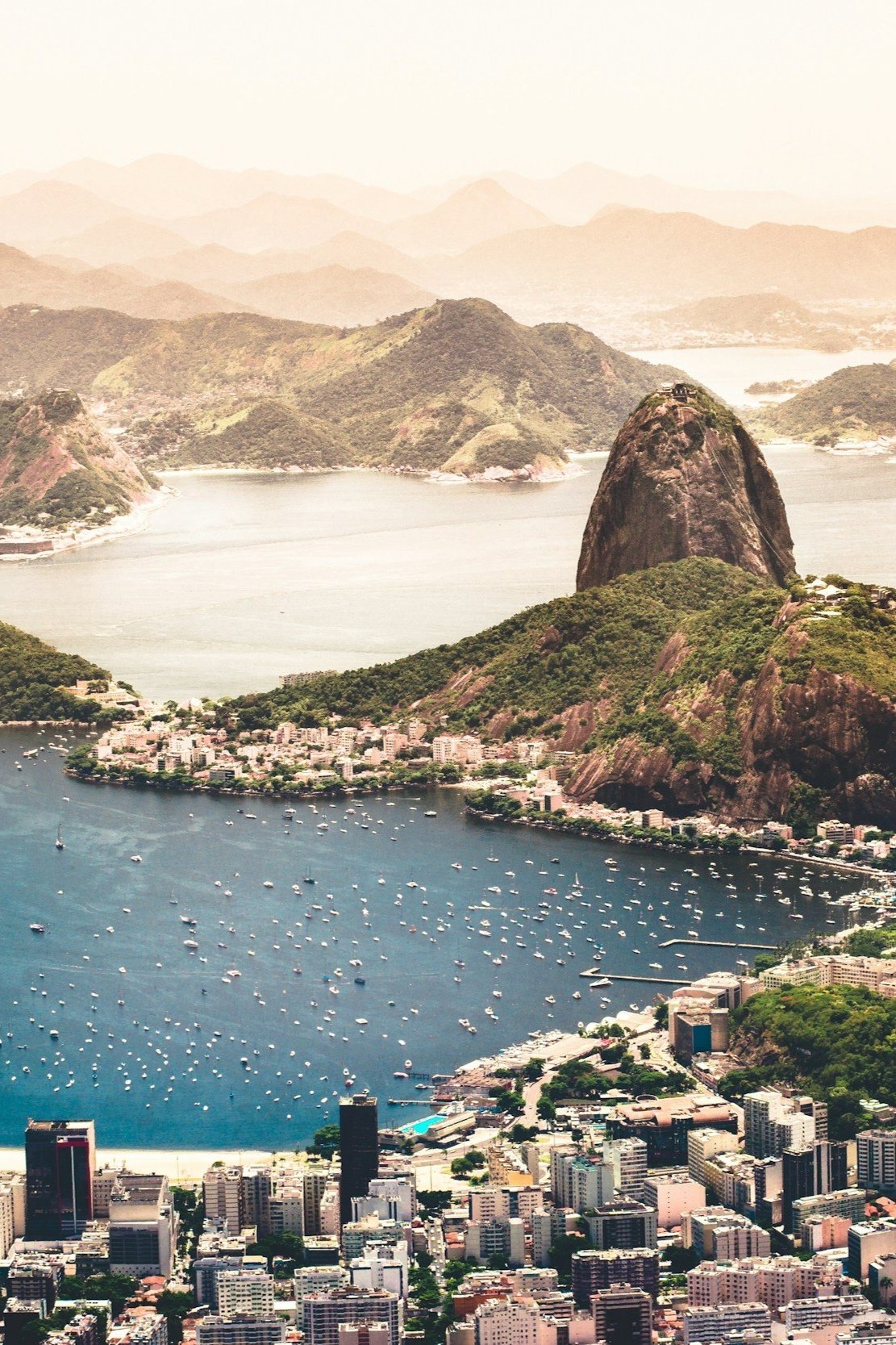 Aerial view of Rio de Janeiro with Sugarloaf Mountain, hills, water, boats, and city buildings.