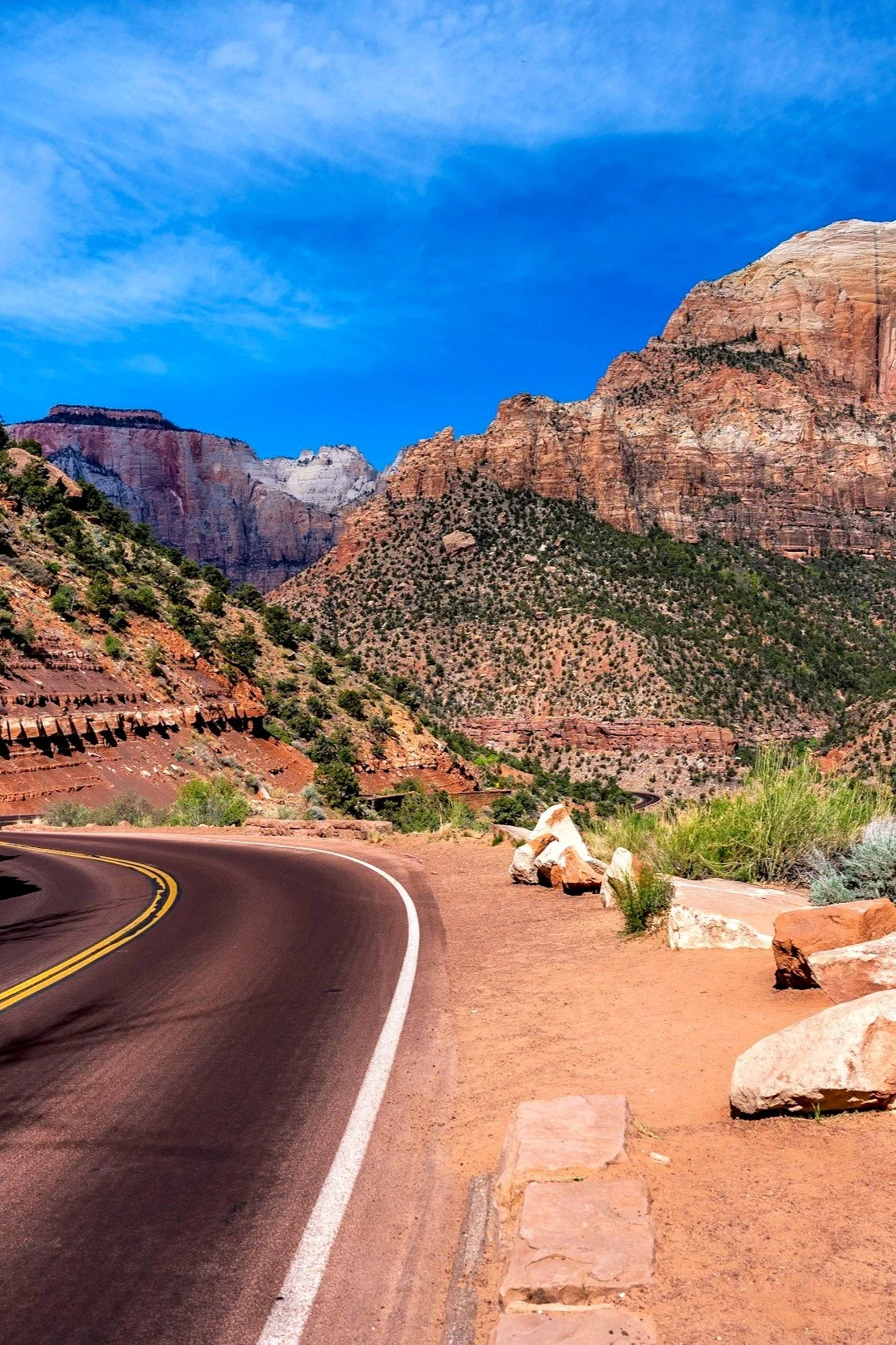 Winding road through the Grand Canyon with red rock cliffs and sparse green vegetation under a blue sky.