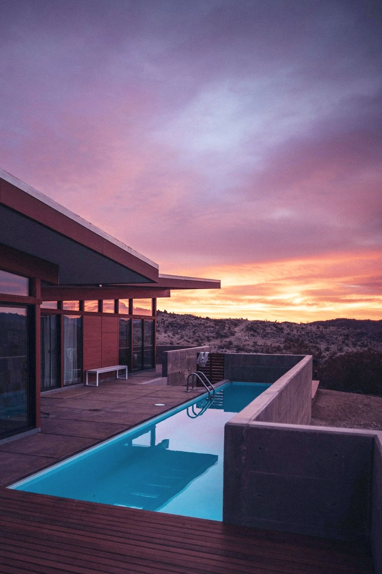 Luxury desert spa with a stunning infinity pool overlooking the arid landscape. Guests relax by the pool, surrounded by elegant lounge chairs and lush desert vegetation, creating a serene oasis atmosphere.