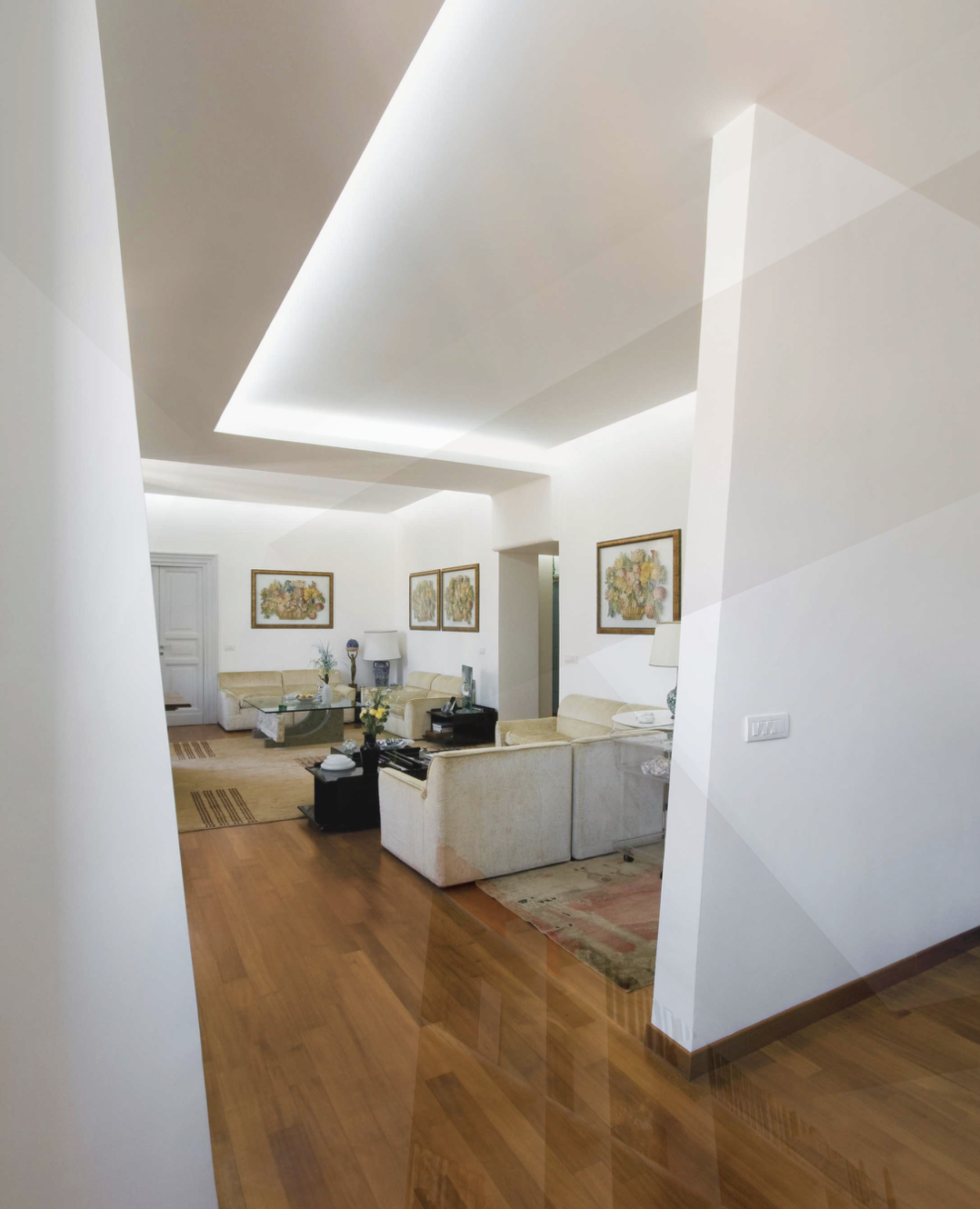 Soggiorno con divani beige, tavolino centrale, quadri alle pareti, lampade e tappeti, pavimento in parquet e giochi di luce