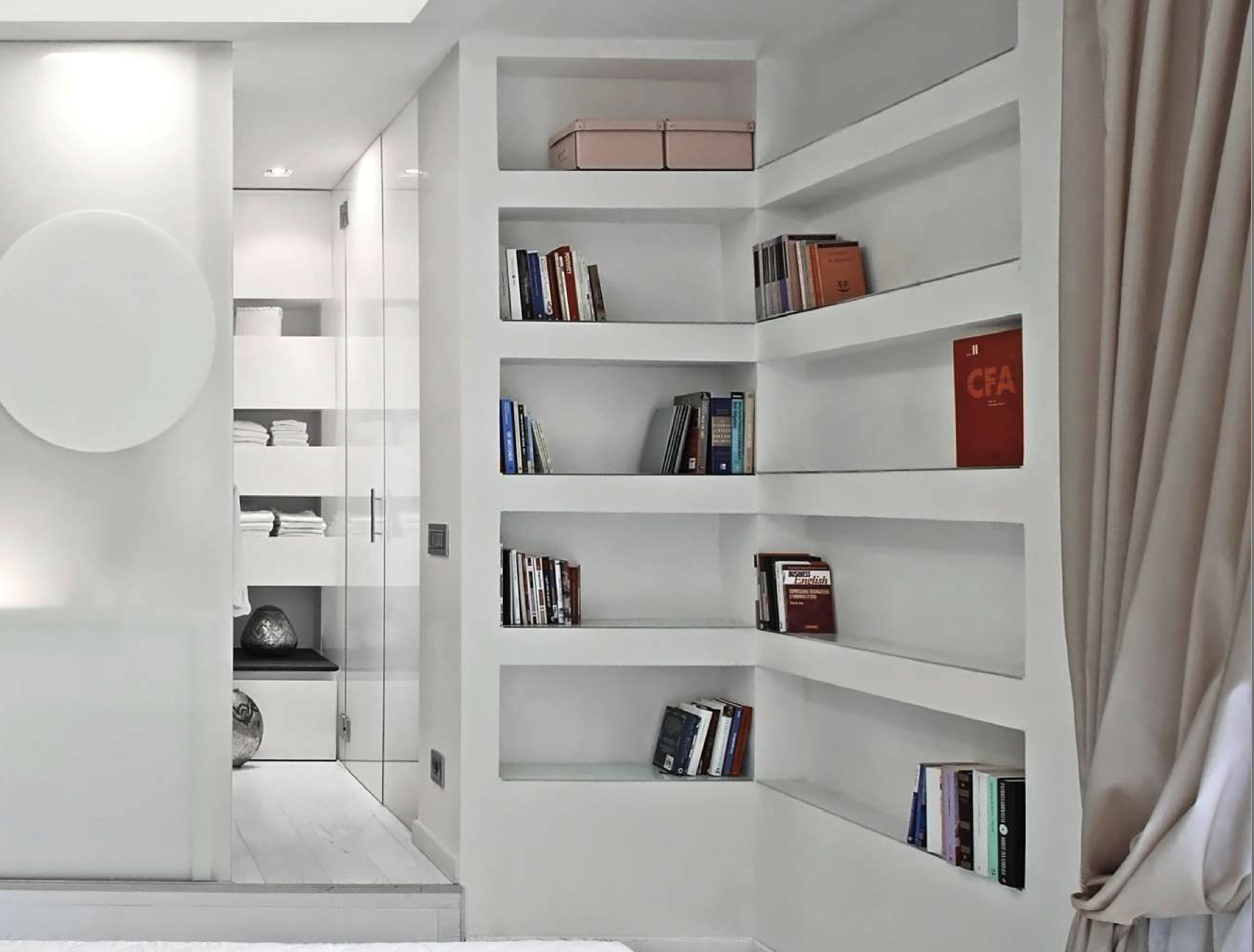 Scaffale bianco con libri e riviste in una stanza moderna con pareti bianche e tende beige