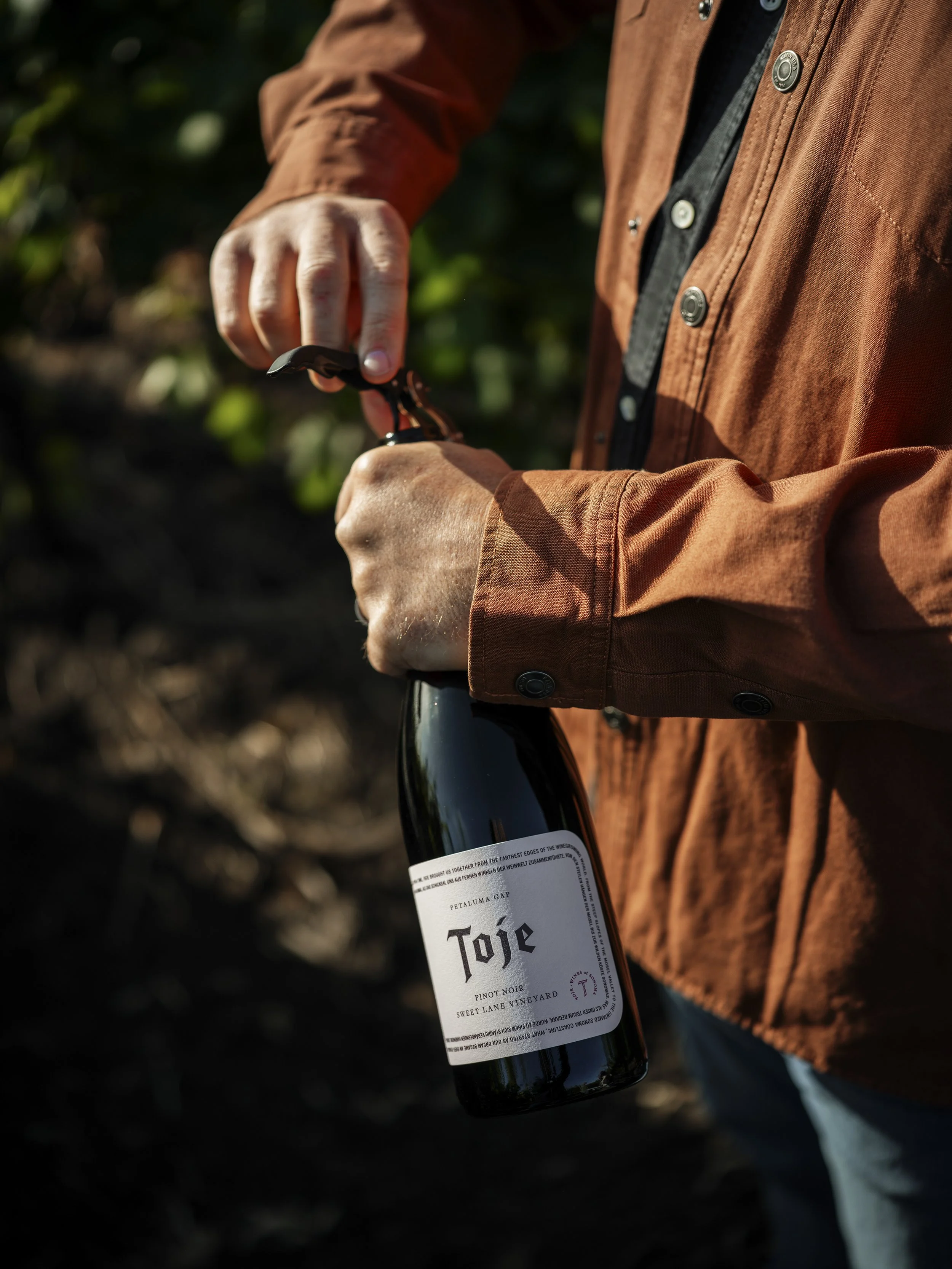 Person in a brown jacket holding a wine bottle outdoors.