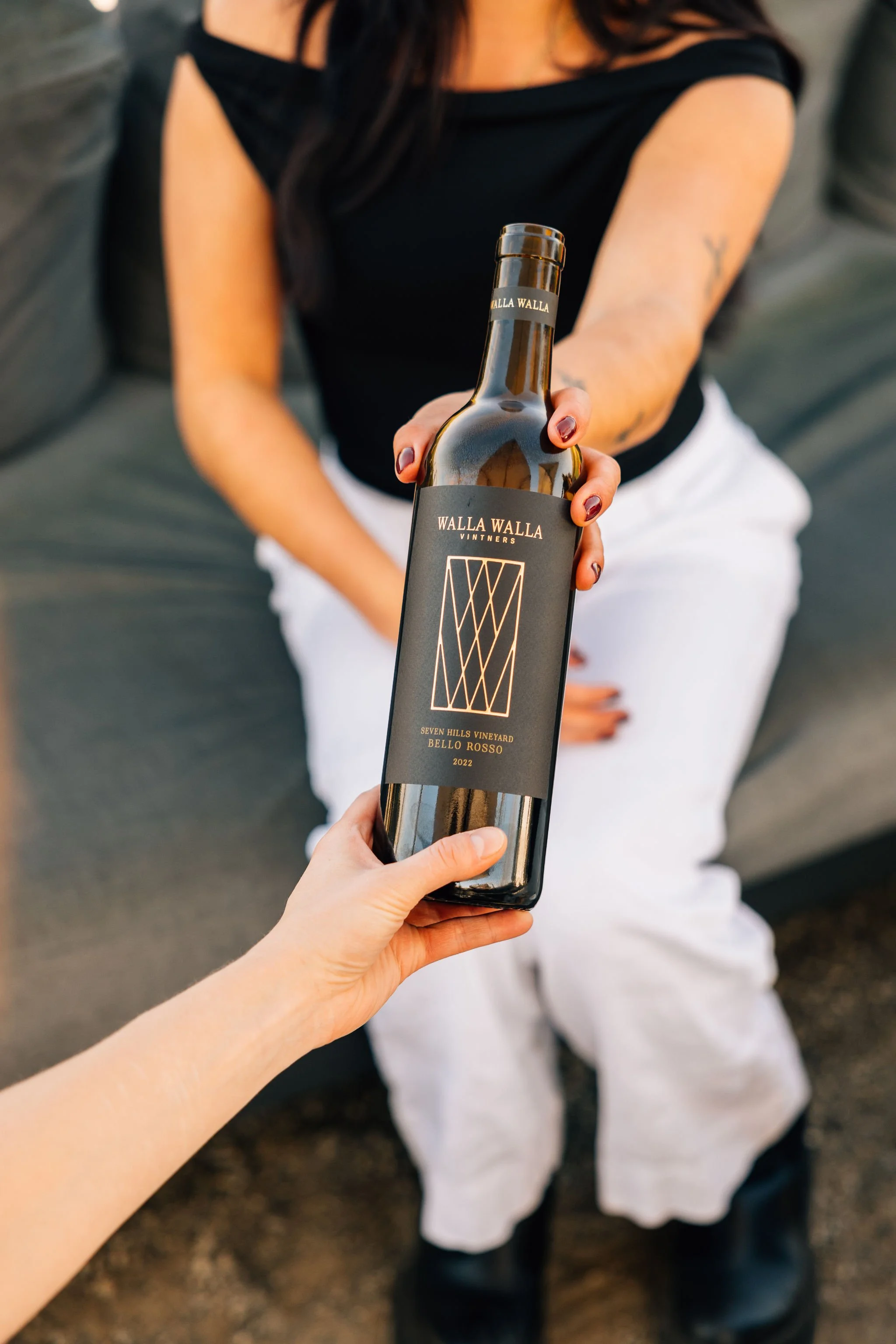 Person holding a bottle of Walla Walla wine extending it toward another person.