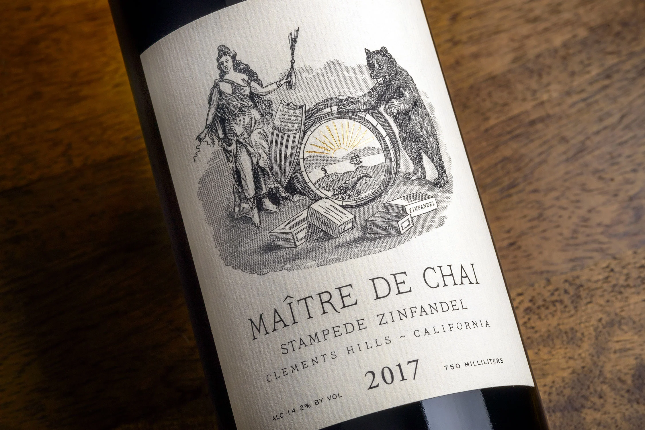 Close-up of a wine bottle label featuring a vintage black-and-white illustration of a woman holding a flag and a bear holding a shield, with a circular emblem depicting a landscape. The label reads "Théâtre de Chai" and includes details about the wine's origin and alcohol content.