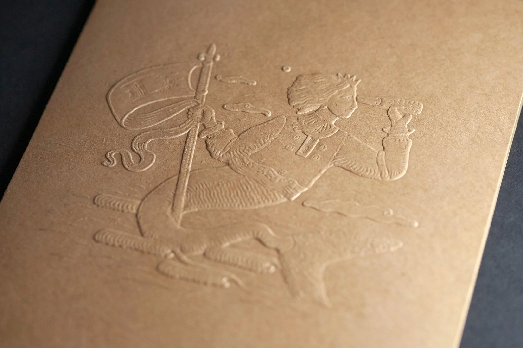Embossed image of a person holding a flag or banner on a textured, gold-colored surface.