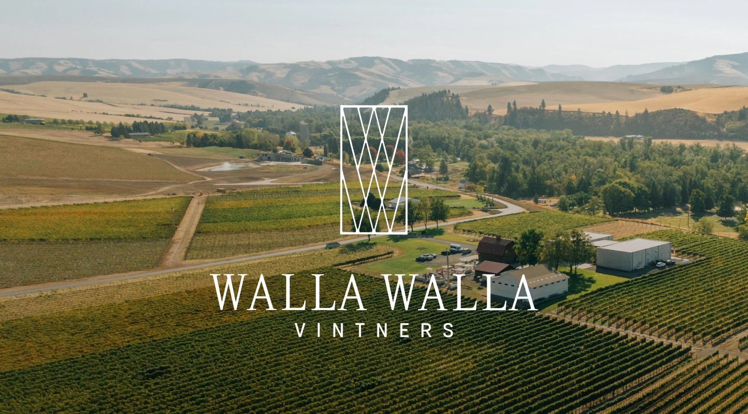 Aerial view of vineyards and farmland in Walla Walla, Washington, with rolling hills in the background, overlaid with a logo and text reading "Walla Walla Vintners."