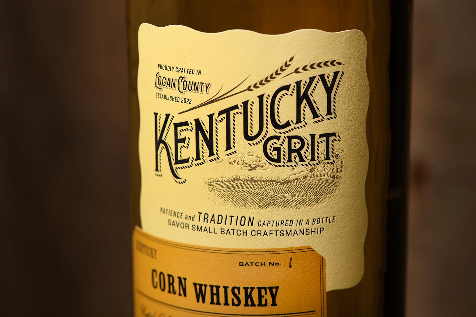 Close-up of a Kentucky Grit bottle label with text about craftsmanship and tradition, featuring a landscape sketch and batch number details.