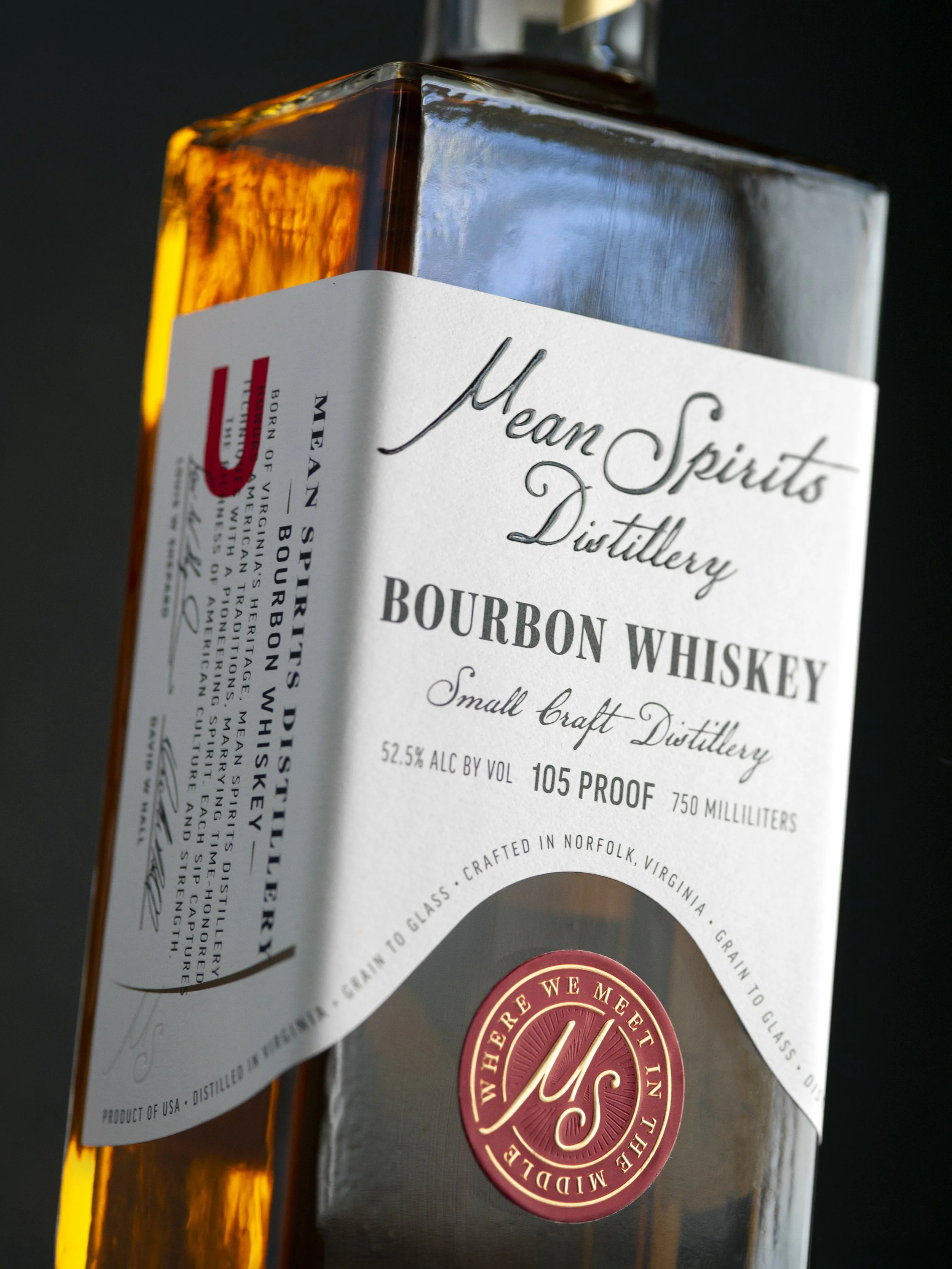 Close-up of a box of Meant Spirits Distillery bourbon whiskey, featuring a white label with black text and a red circular emblem.