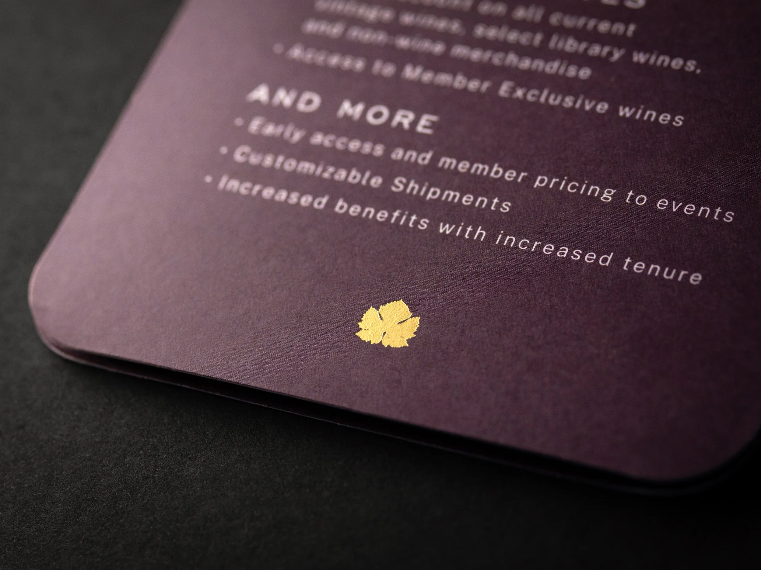 Close-up of a purple paper with white printed text and a small yellow flower illustration at the bottom. The text discusses wine benefits and membership details.