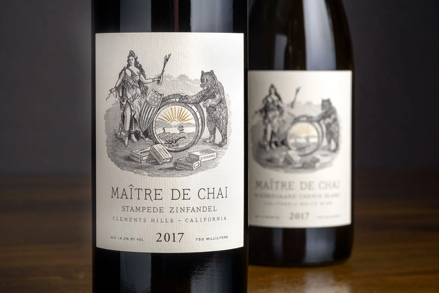 Two bottles of Maître de Chai Stampede Zinfandel wine from Clements Hills, California, vintage 2017, on a wooden surface against a dark background.