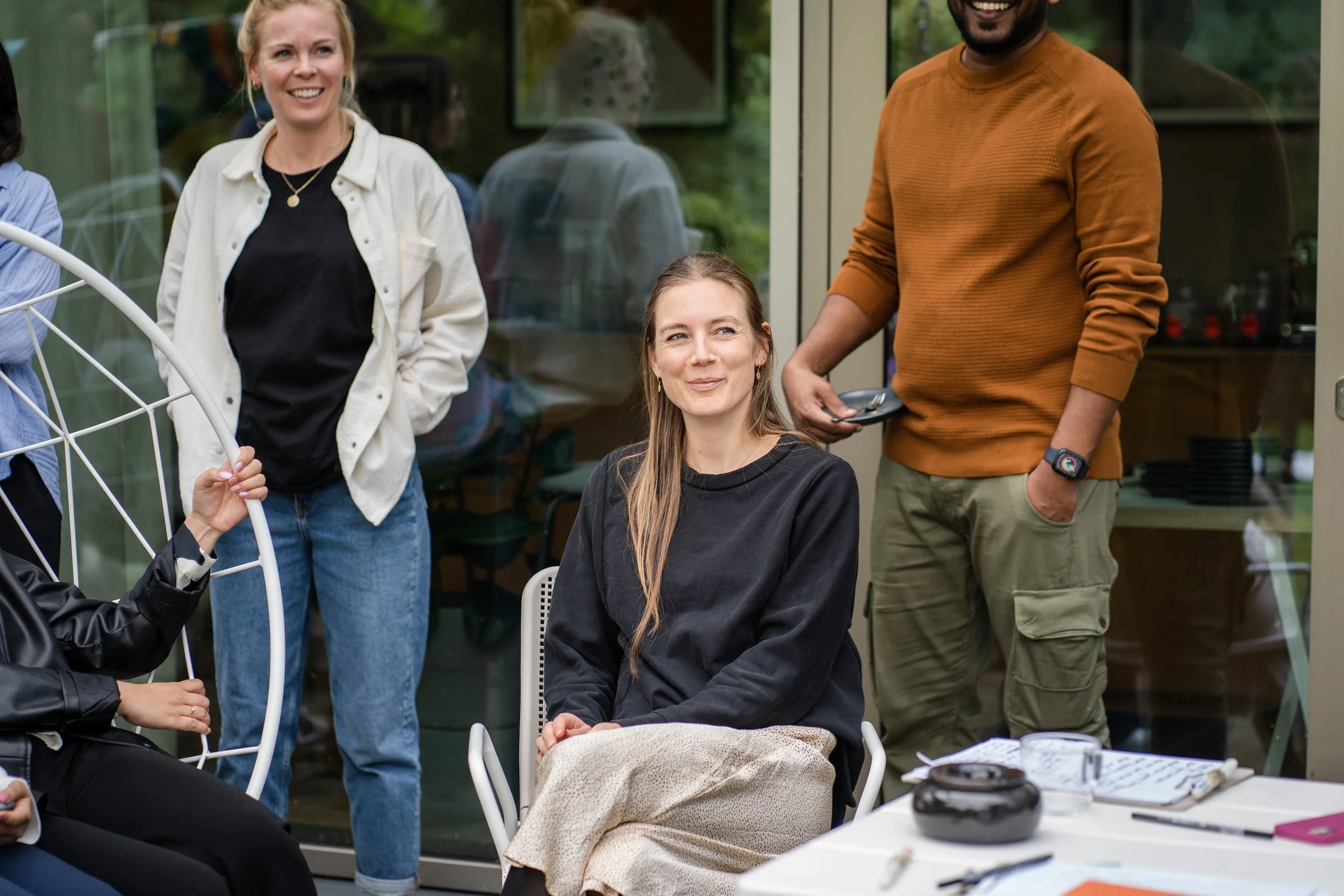 Eine Teilnehmerin hört lächelnd zu, während Kolleg:innen hinter ihr stehen, in einer Teamcoaching-Session im Freien
