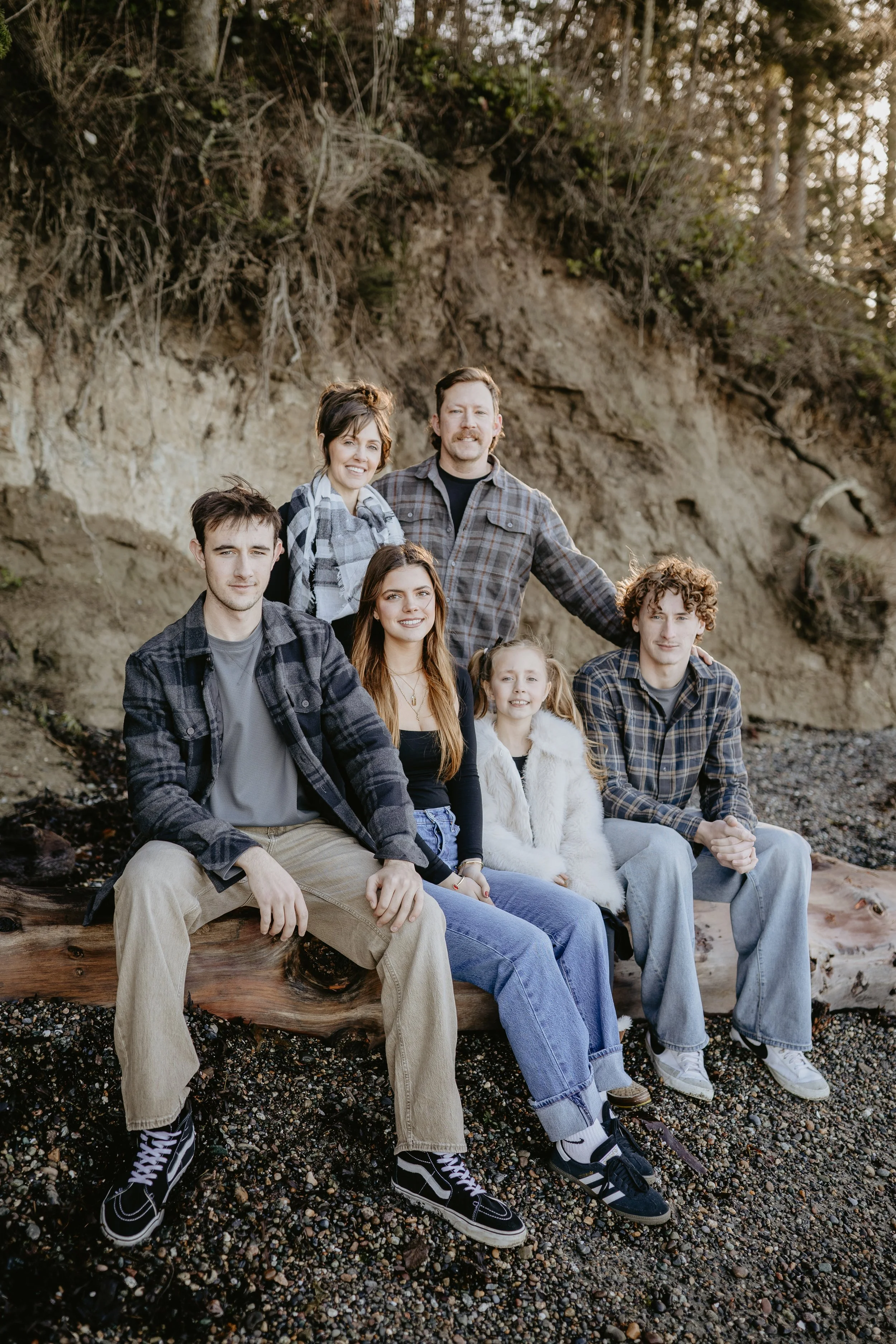 A family of four with a dog on a beach near water, smiling and posing for a photo.