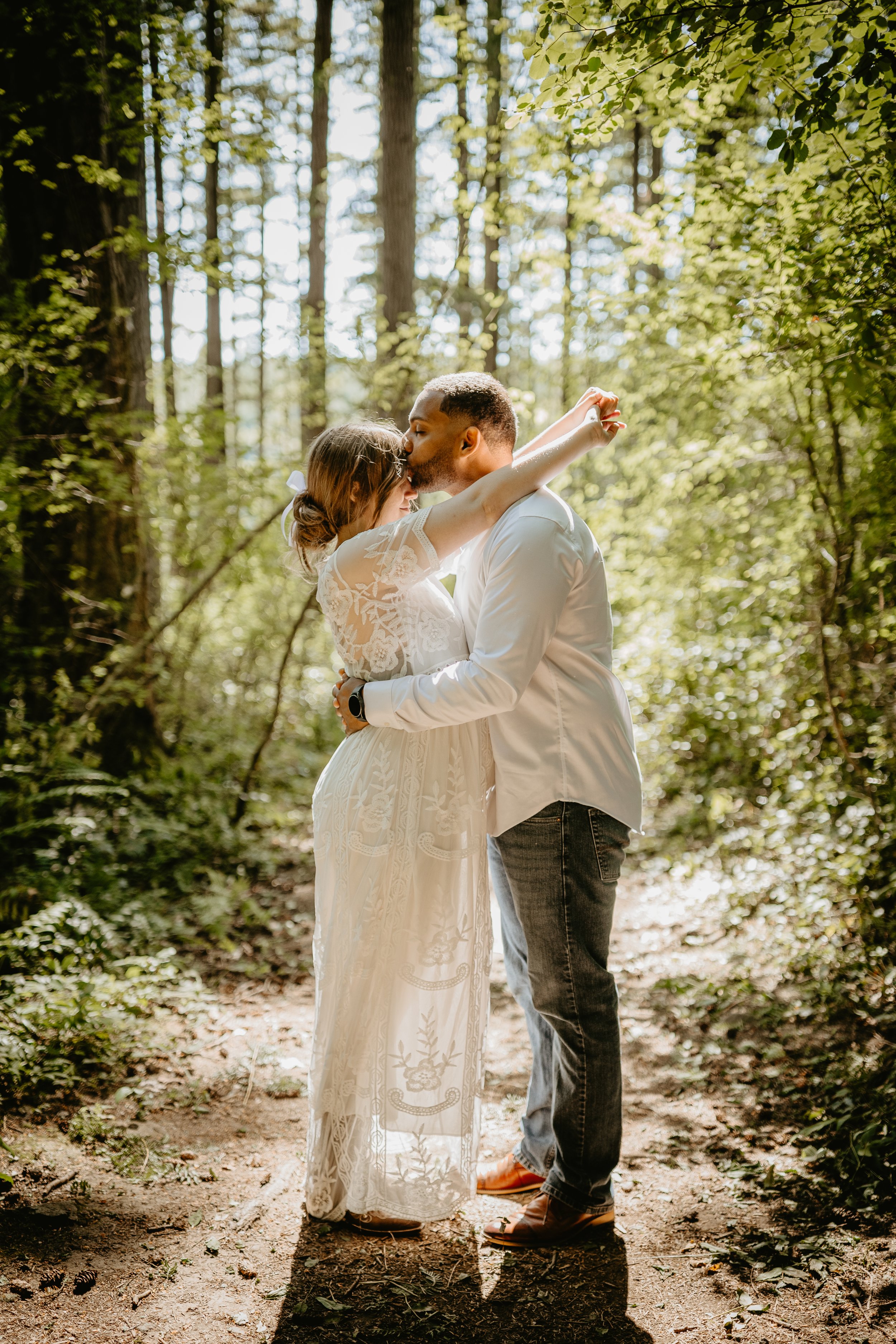 A happy couple outdoors, smiling and embracing each other on sunny day, with greenery in the background.