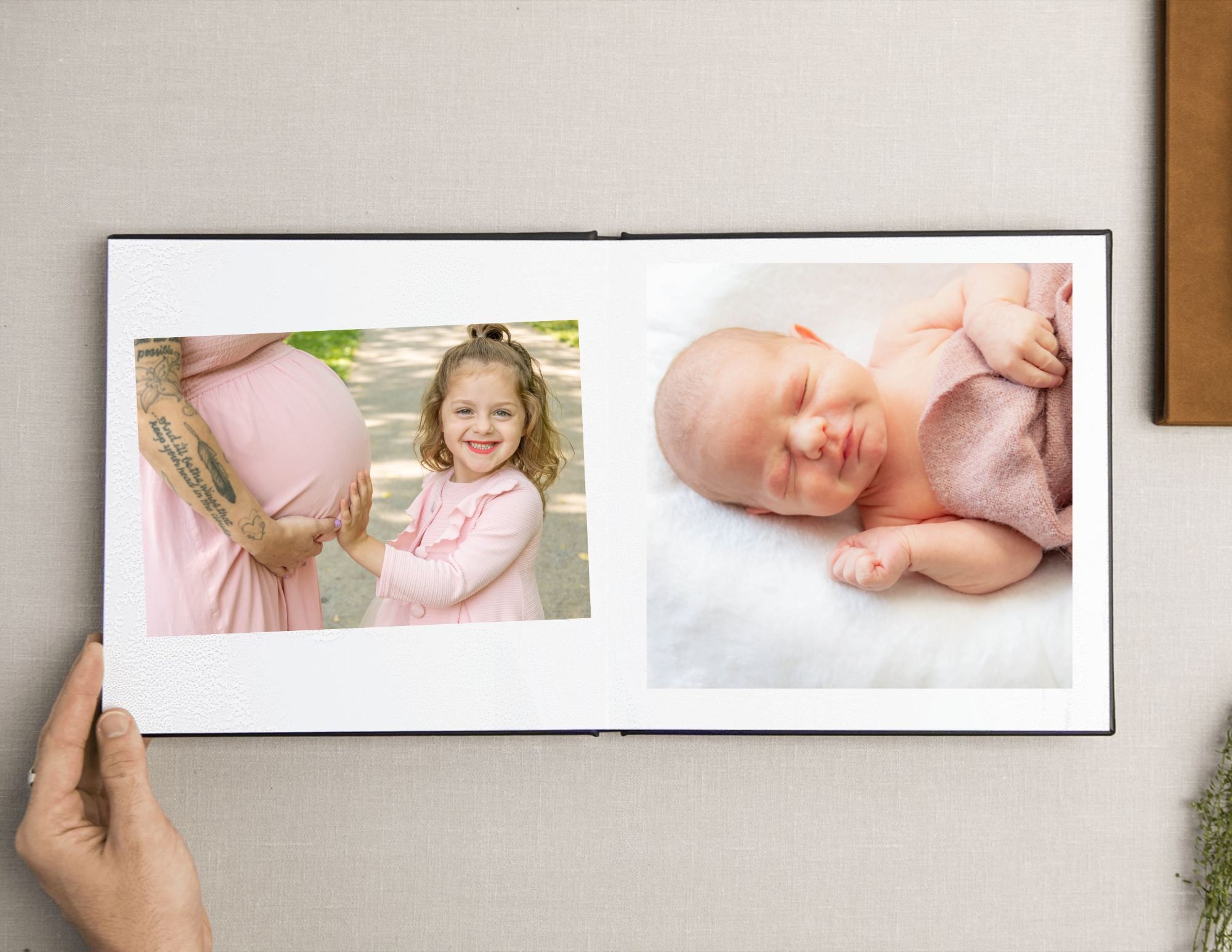 Photograph of a photo album with two pictures: one of a pregnant woman holding hands with a young girl outdoors, and the other of a sleeping newborn baby wrapped in pink clothing.