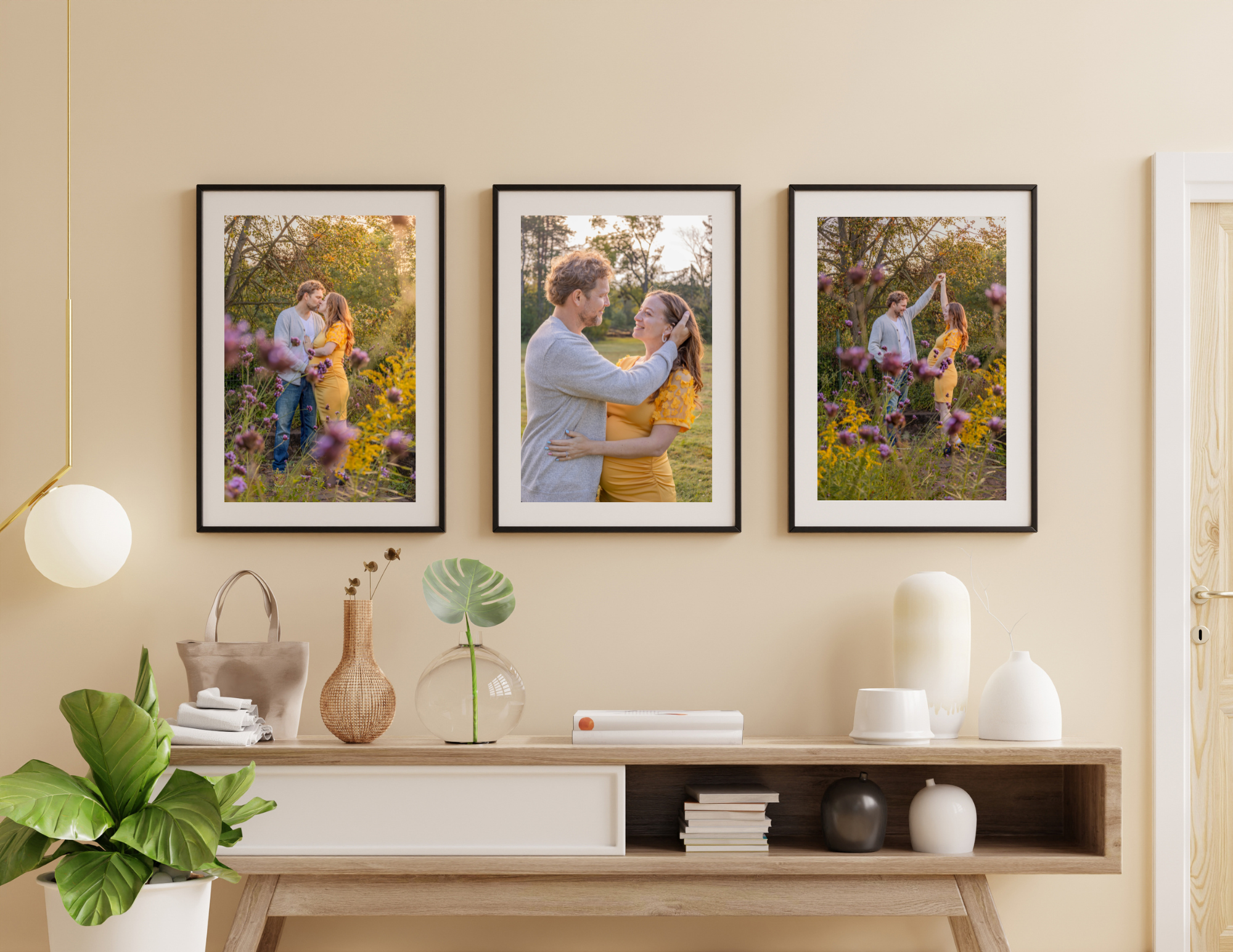 A wall decorated with three framed photos showing a couple embracing in a field of colorful flowers during sunset. The furniture below includes a light wood sideboard with various vases, books, and plants on and around it.
