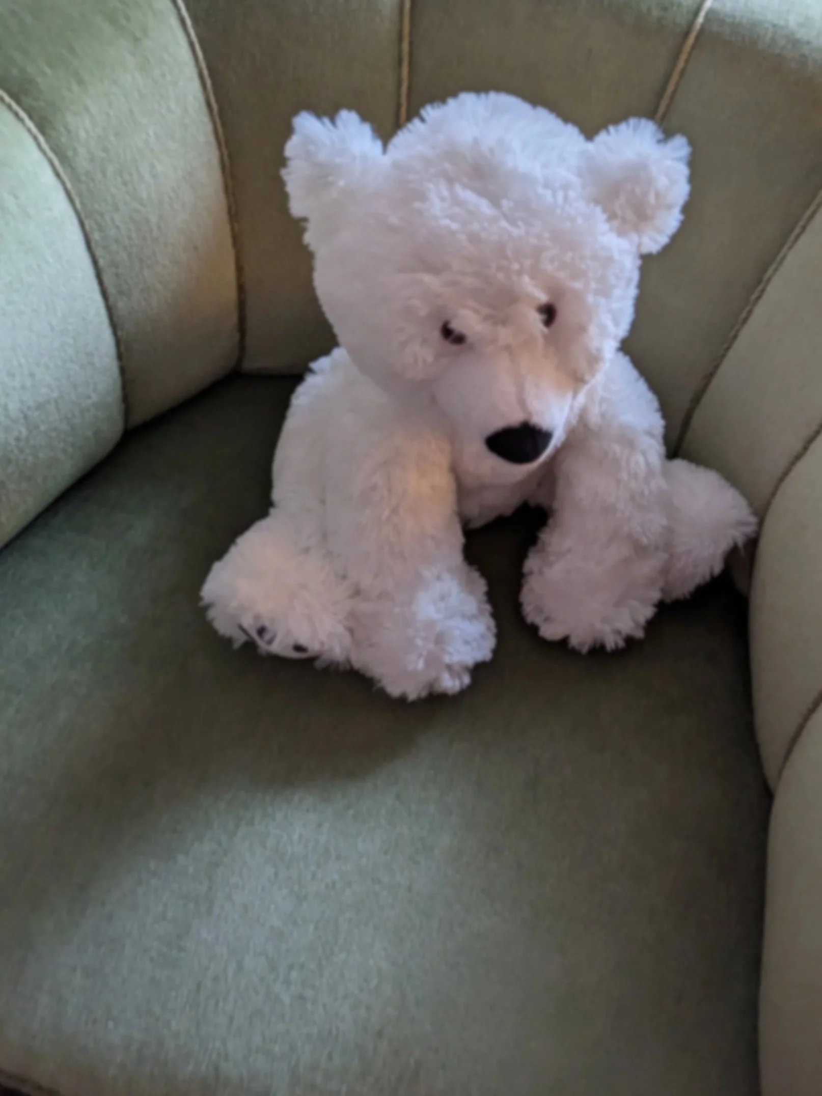 A white plush teddy bear sitting on a green upholstered couch.