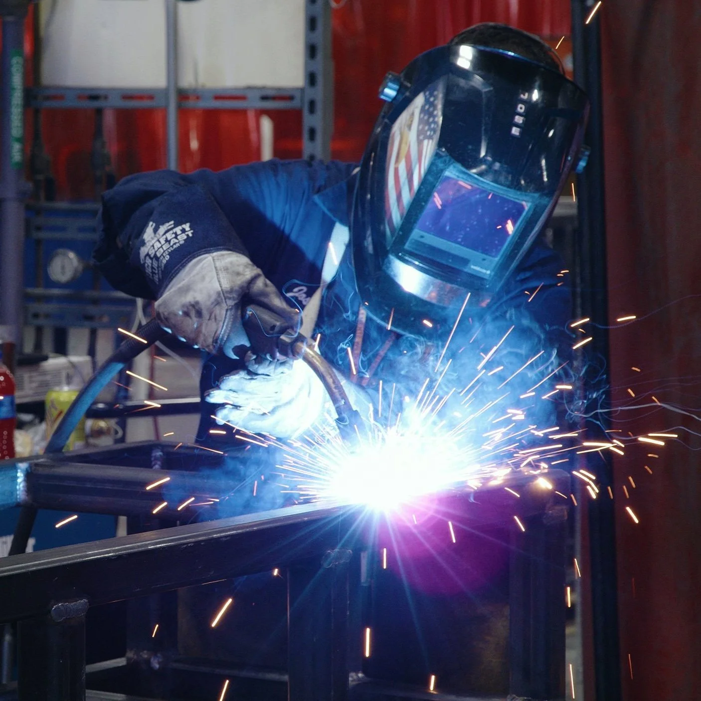 A welder wearing protective gear welding metal with sparks flying in a workshop.