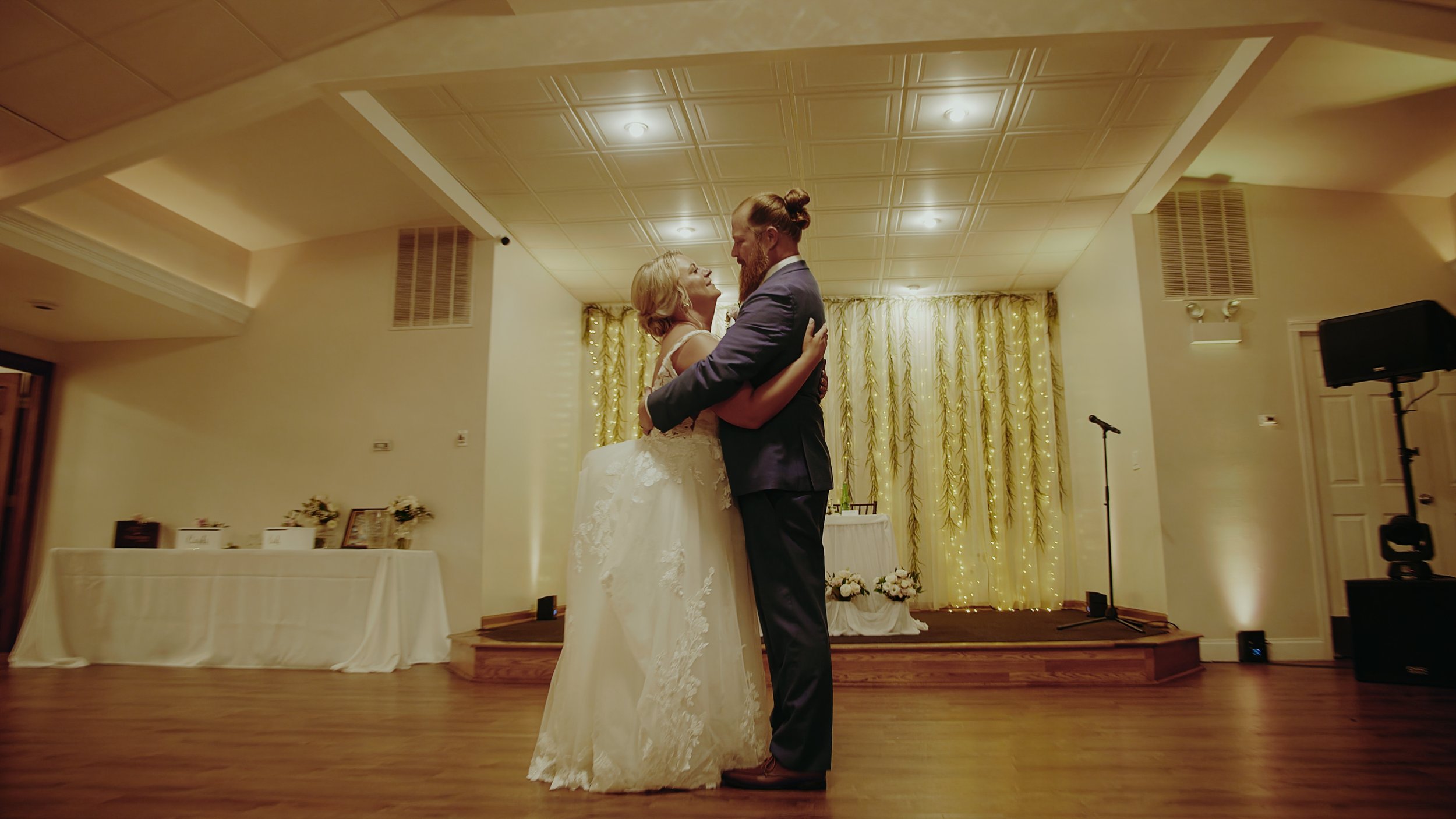 A bride and groom embrace during their wedding dance in a decorated reception hall.