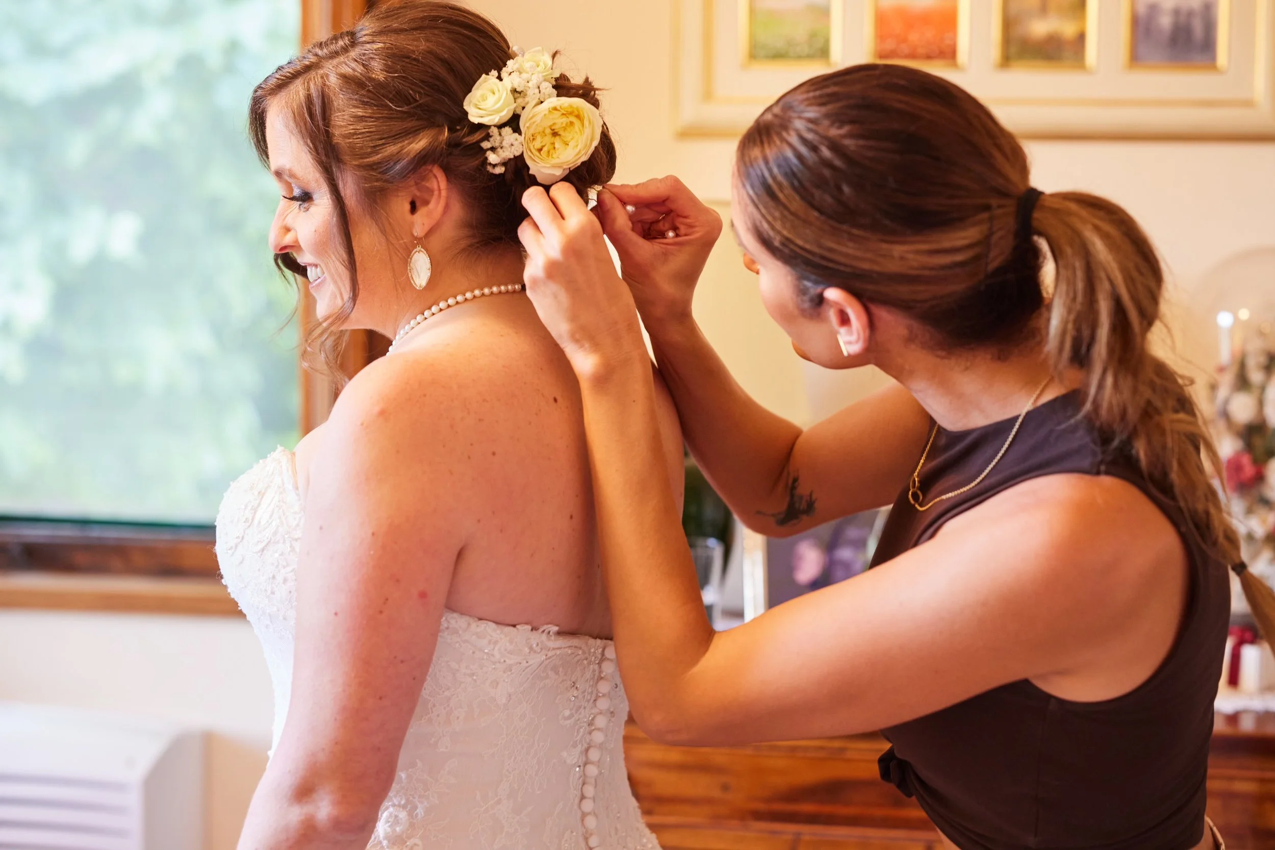 A woman in a wedding dress smiling as another woman pins a flower arrangement in her hair.