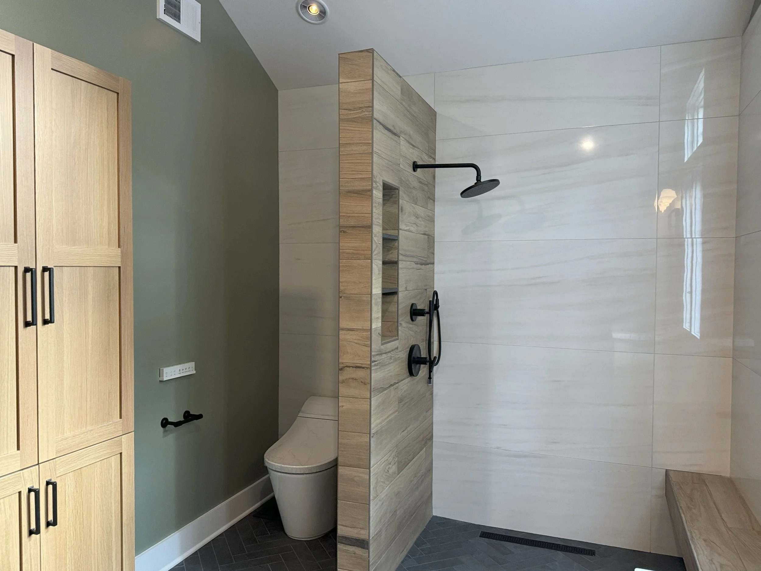 Modern bathroom with beige cabinetry, a toilet, a walk-in shower with black fixtures, and light-colored tiled walls.