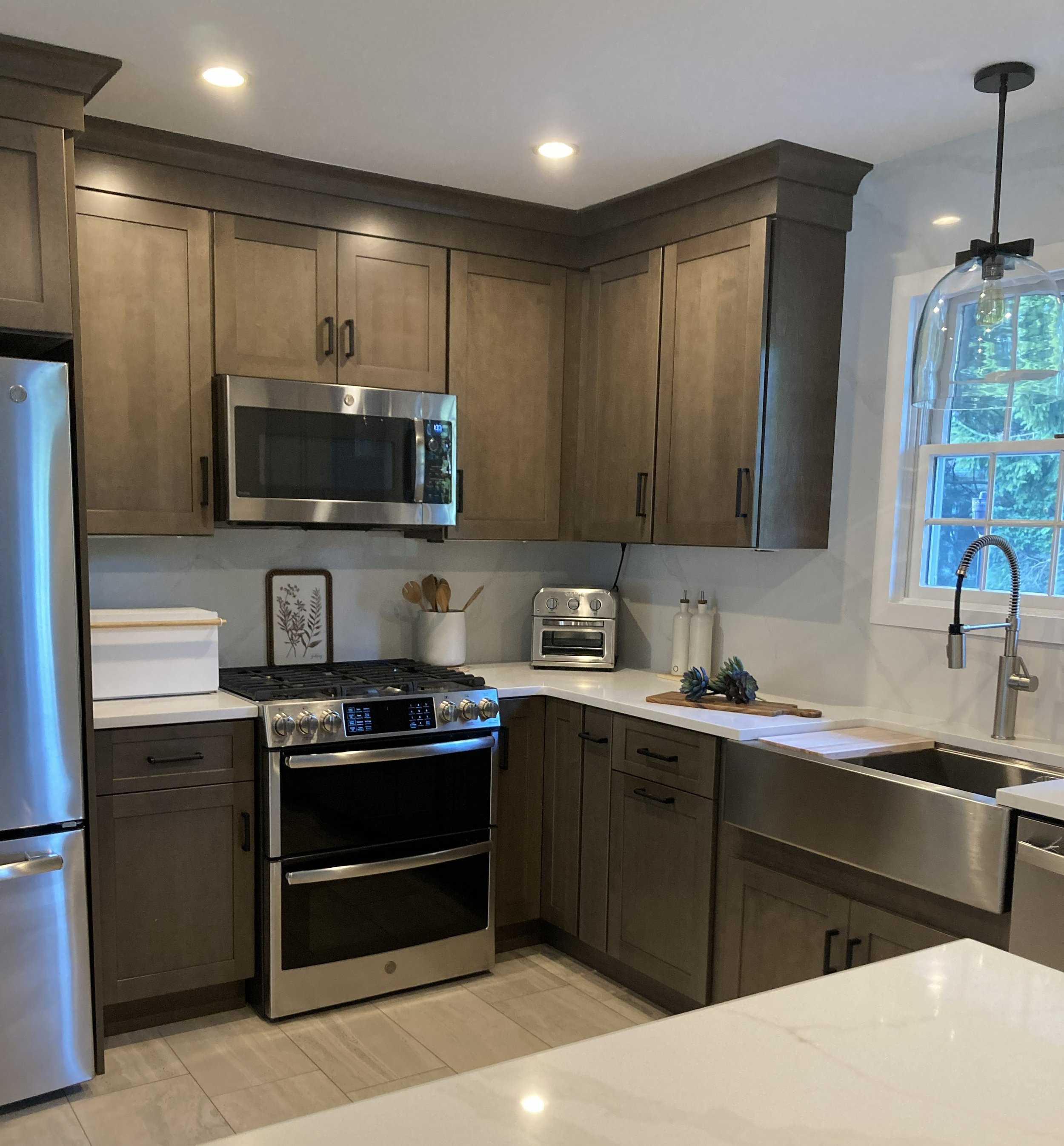 Modern kitchen with wooden cabinets, stainless steel appliances, white countertops, and a large sink near a window.