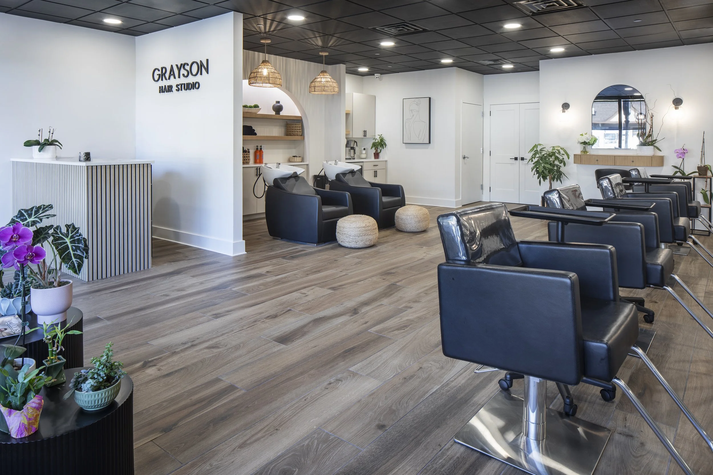 Interior of a modern hair salon with black styling chairs, hair washing stations, and decorative plants.
