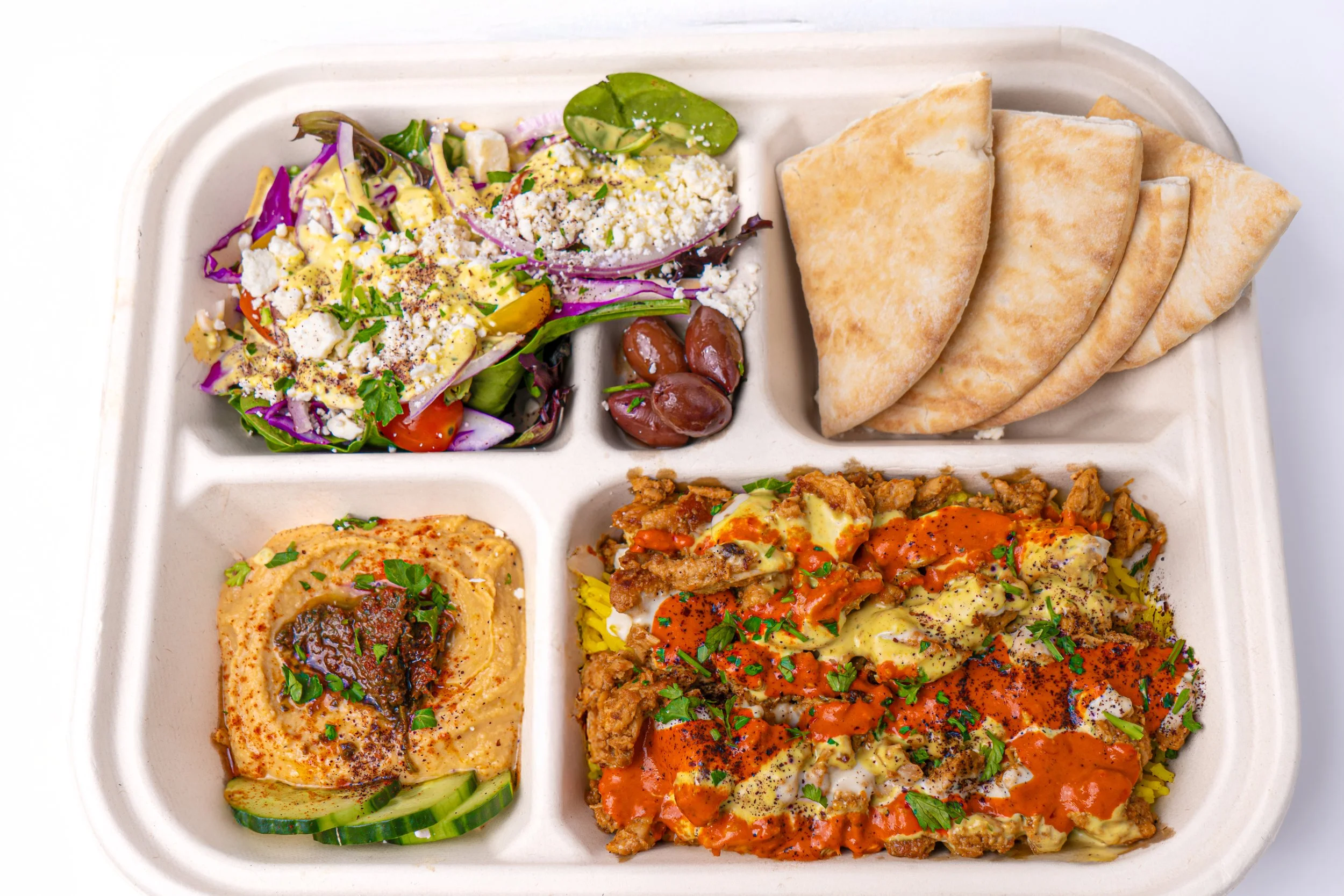 A divided meal tray with a salad, beans, flatbread, hummus, and a casserole topped with sauce and herbs.