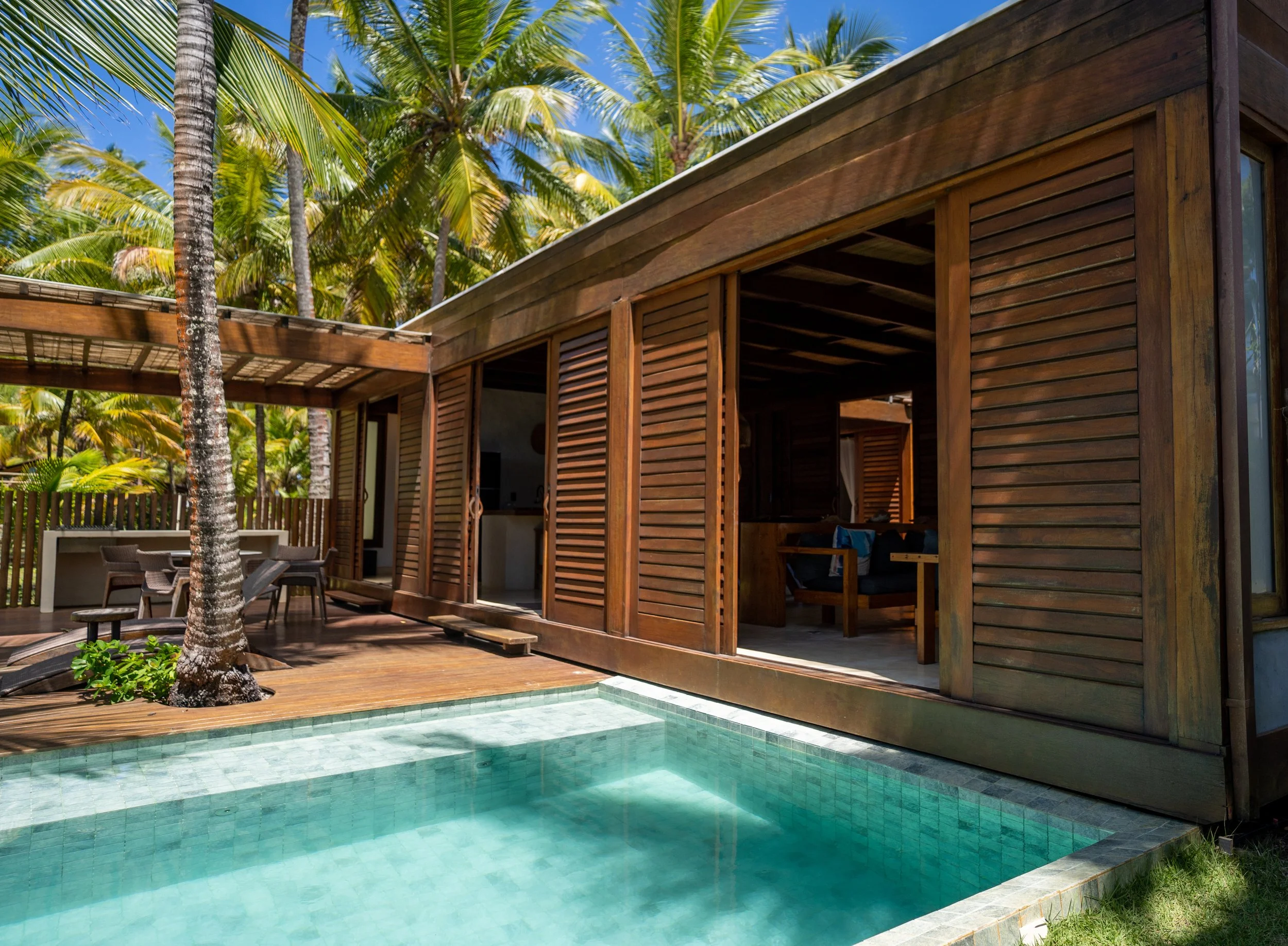 Casa de madeira com piscina e palmeiras ao fundo.