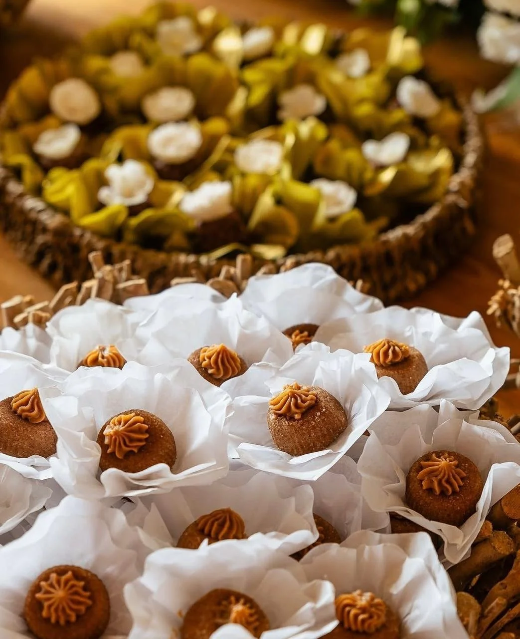 Doces típicos brasileiros, doces de batata-doce com cobertura de doce de leite, apresentados em forminhas de papel branco e dispostos em uma bandeja de palha.