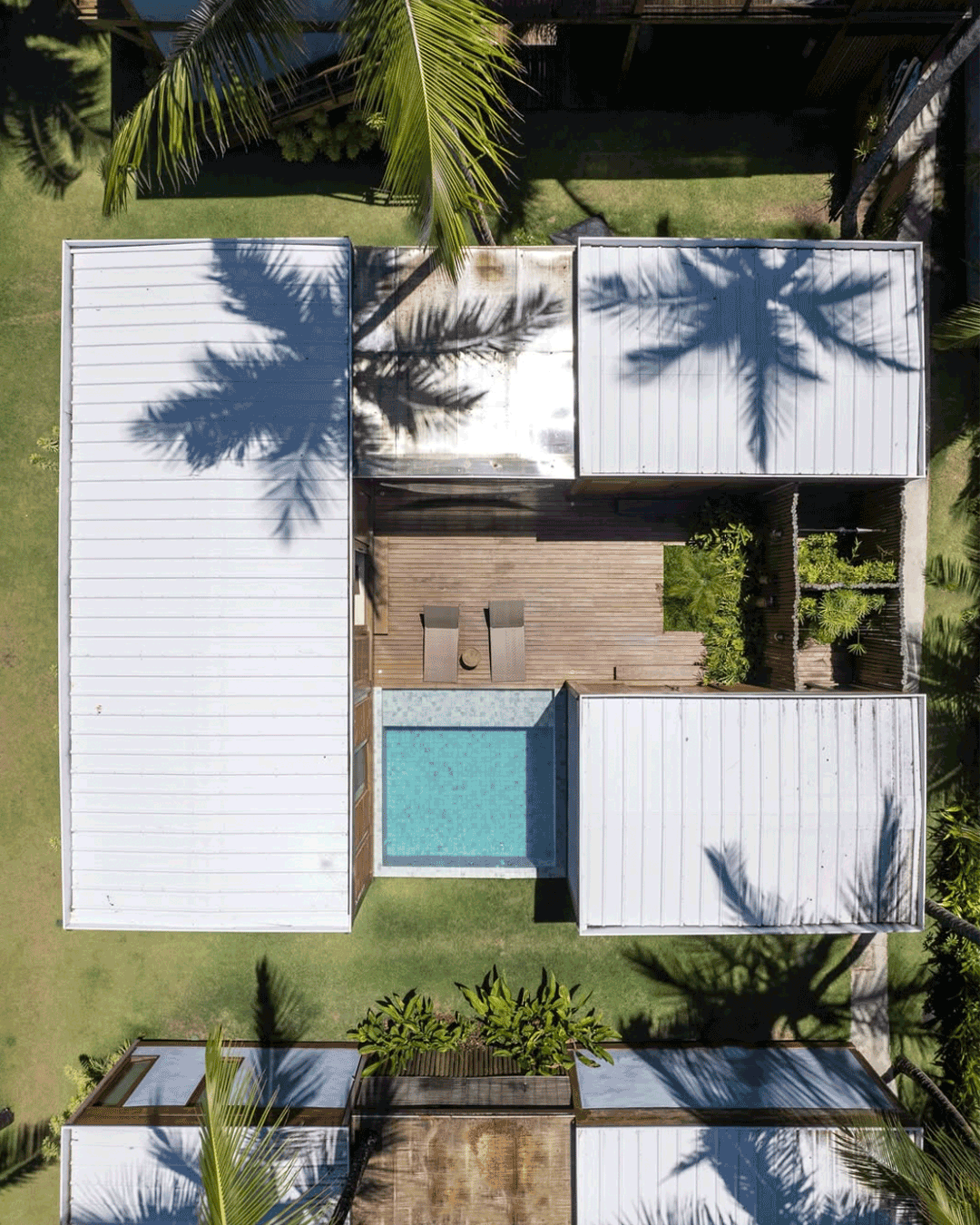 Vista aérea de uma casa de arquitetura moderna com telhado de metal, piscina no pátio e bastante vegetação ao redor, incluindo árvores e plantas tropicais.