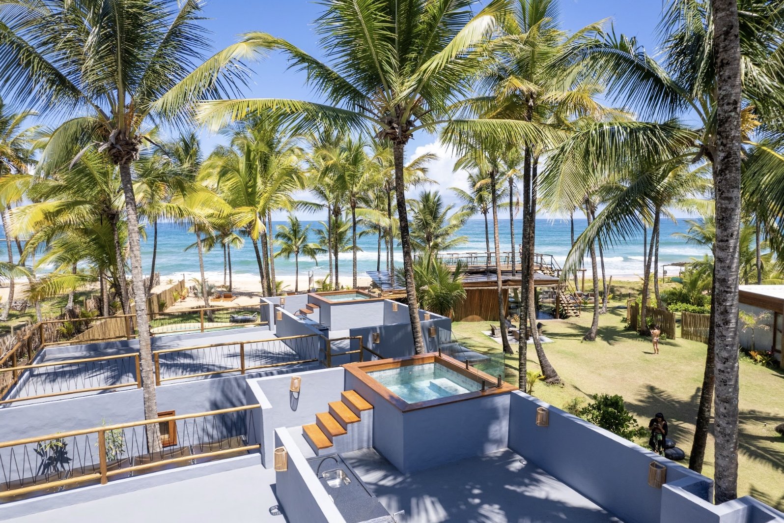 Vista de um resort na praia com árvores de palmeira, piscinas e vista para o mar