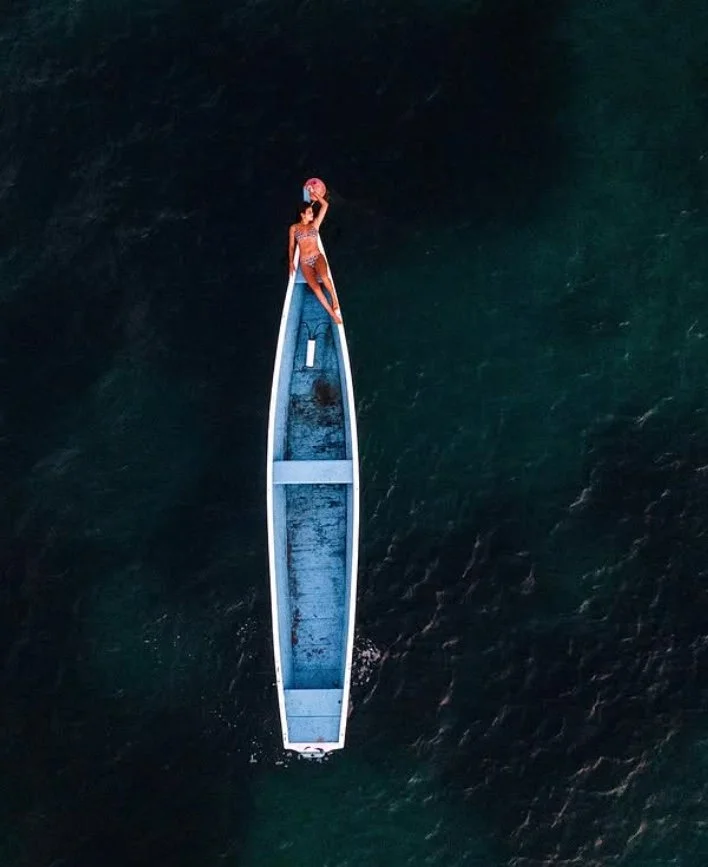 Pessoa em pé em uma canoa no mar, segurando uma bola de praia