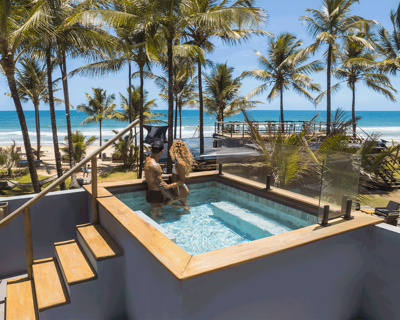 Casal no jacuzzi com vista para a praia e árvores de palmeira ao fundo